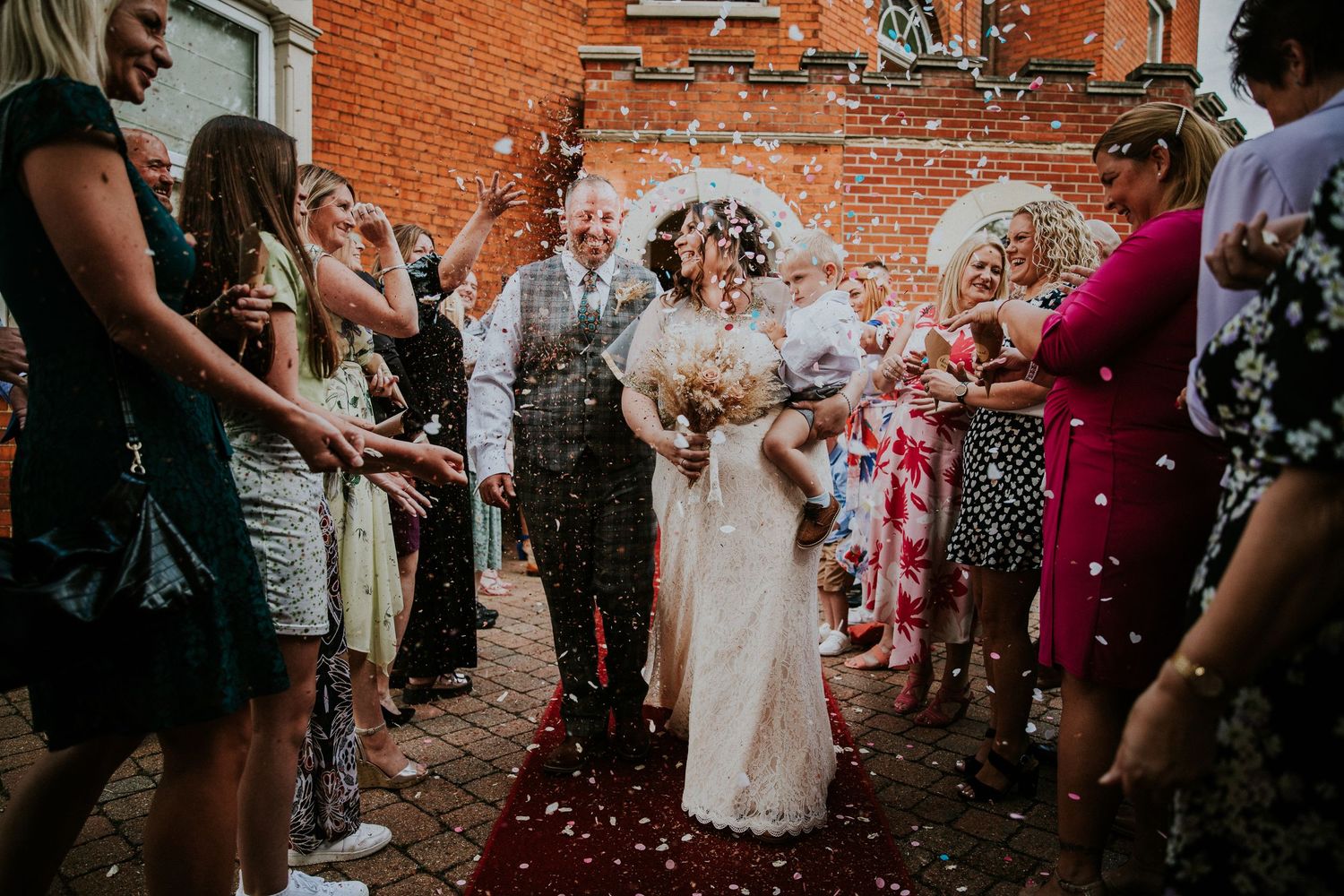 Wedding celebration with confetti being thrown against a rustic brick wall backdrop.