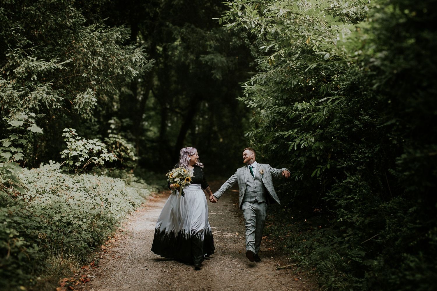 Couple walking hand in hand down a forest path in wedding attire.