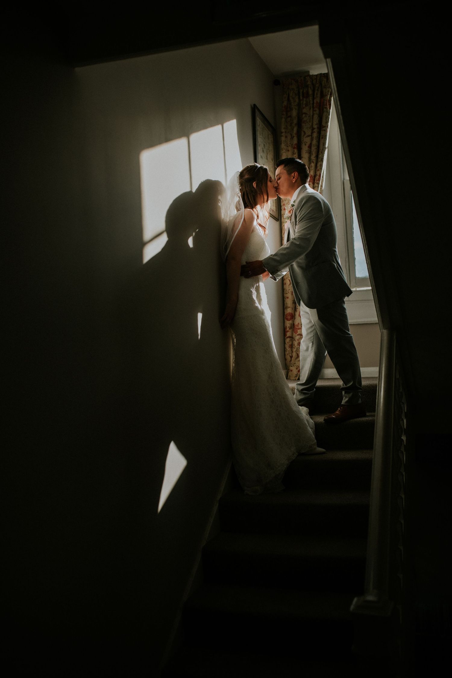 A dramatic silhouette of a couple sharing an intimate moment on a staircase with natural light casting shadows.
