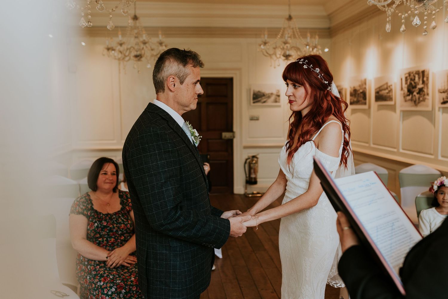 Wedding ceremony taking place in elegant room with chandelier and white decor.