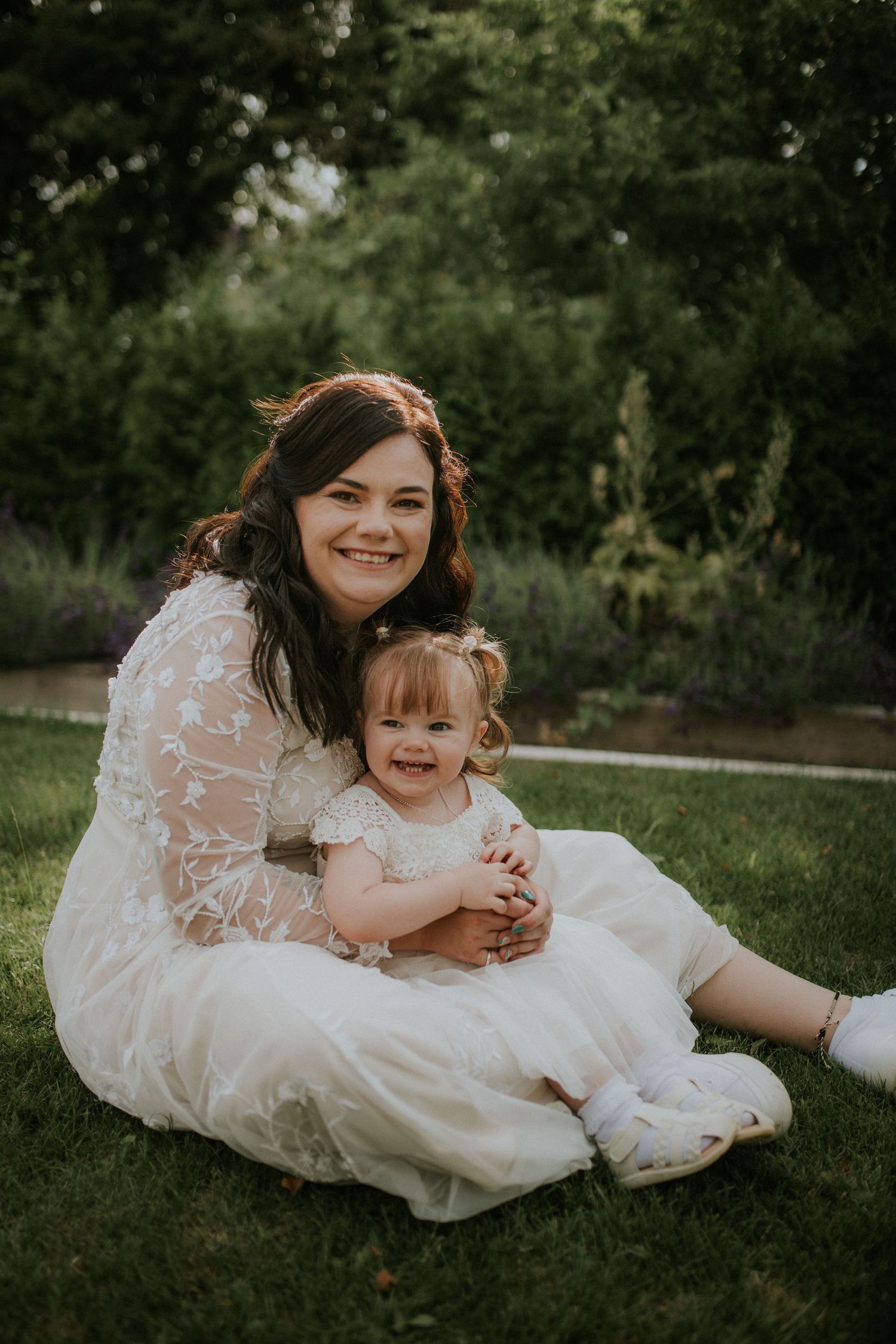 Joyful wedding moment captured on grass with white lace dresses and natural lighting.