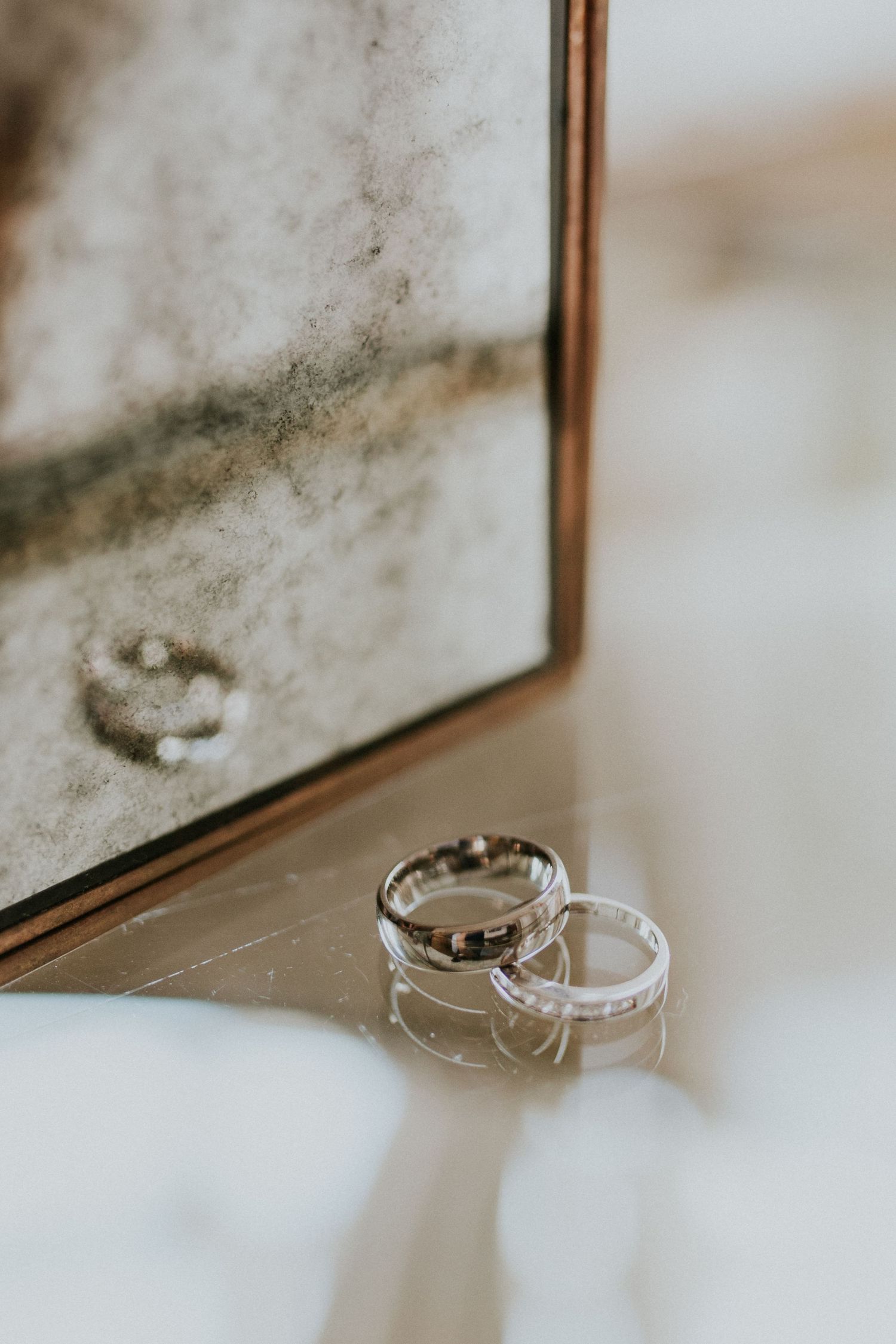 Two wedding rings casting reflections on a mirrored surface in soft, natural light.