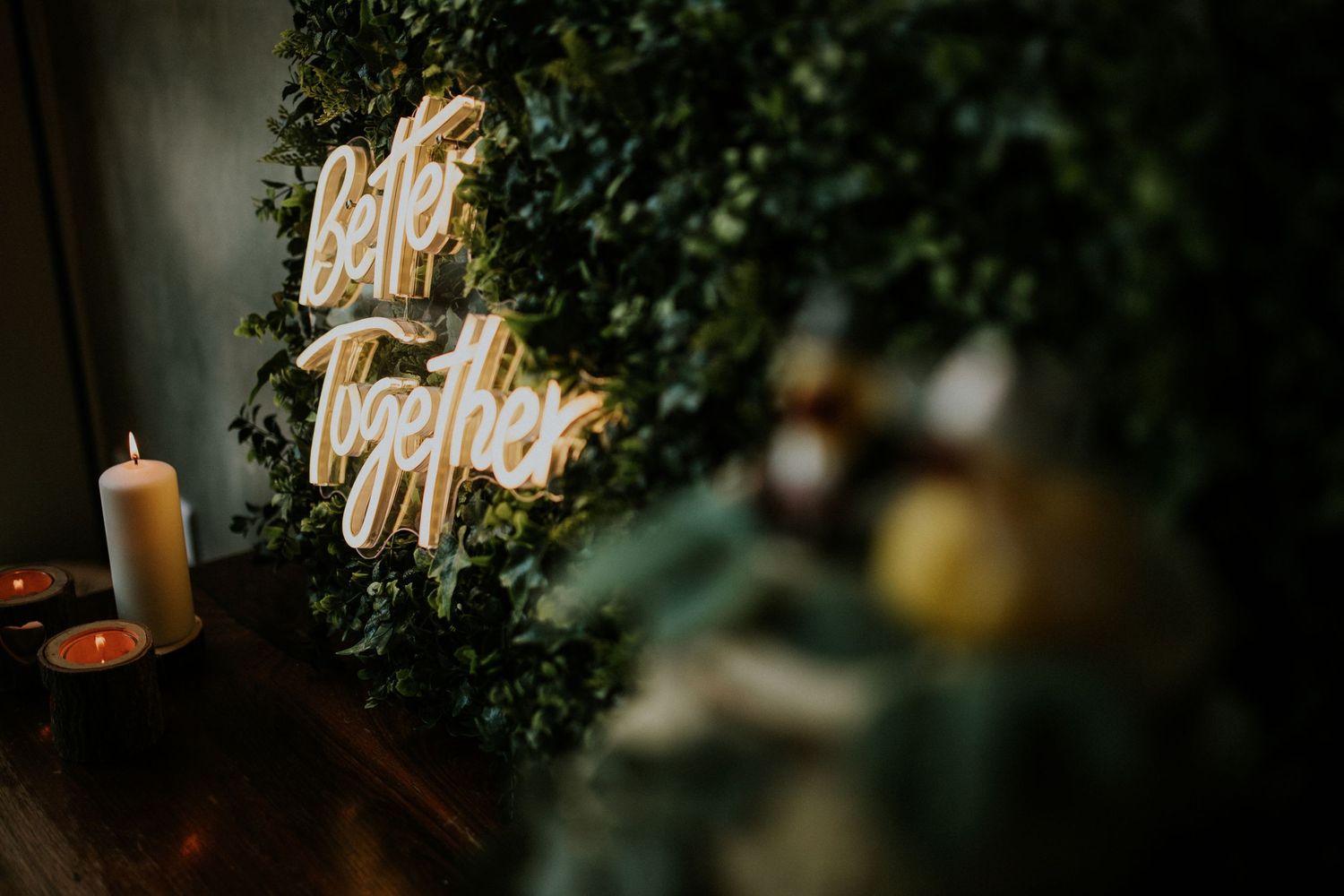 Illuminated 'Better Together' neon sign displayed against greenery at a wedding.