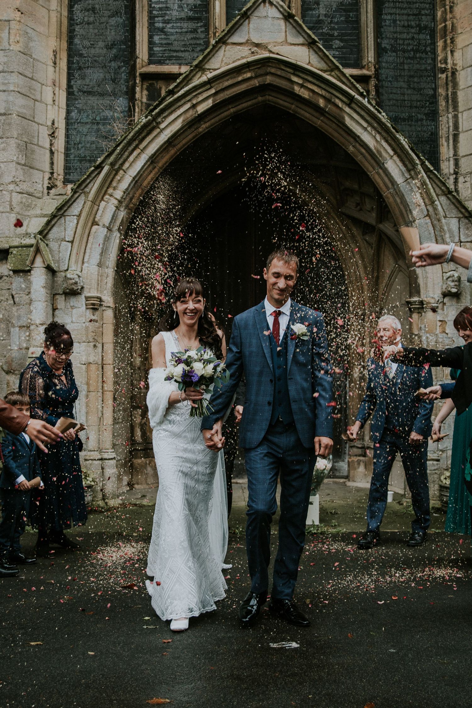 Joyful newlyweds exit church while guests throw confetti in celebration.