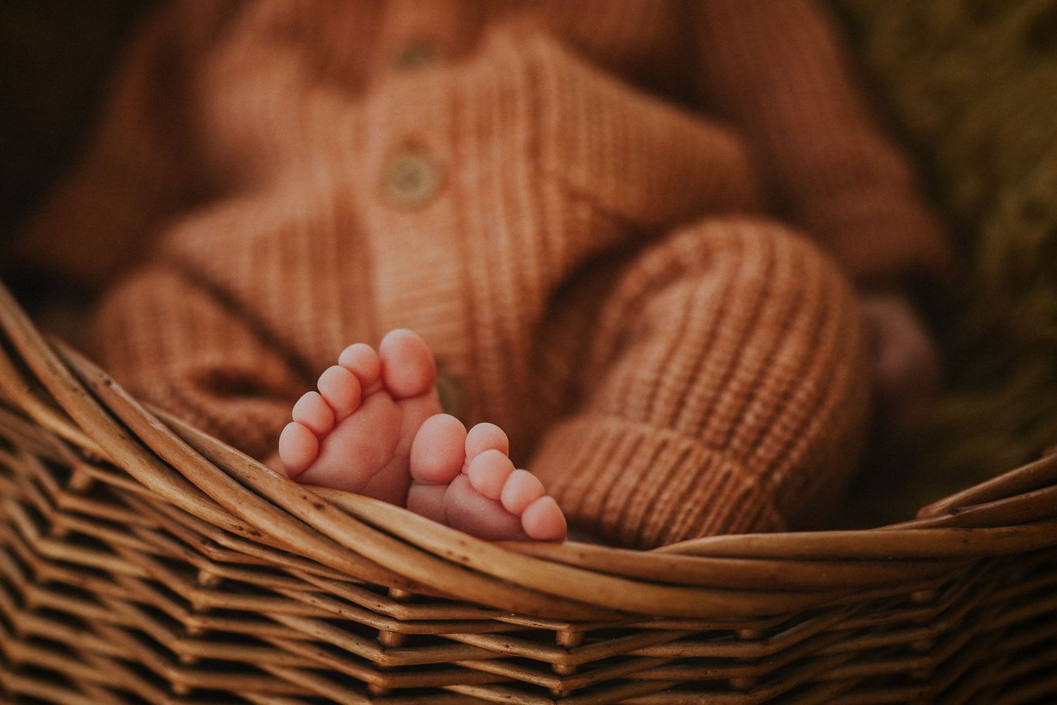 Tiny baby feet rest in a cozy woven basket with warm lighting and brown tones.