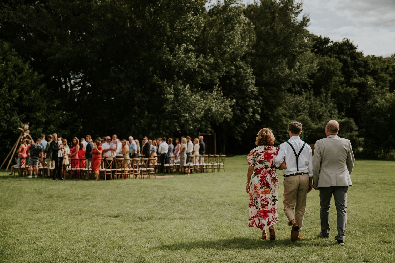 Wedding party walks across green lawn towards seated guests at outdoor ceremony venue.