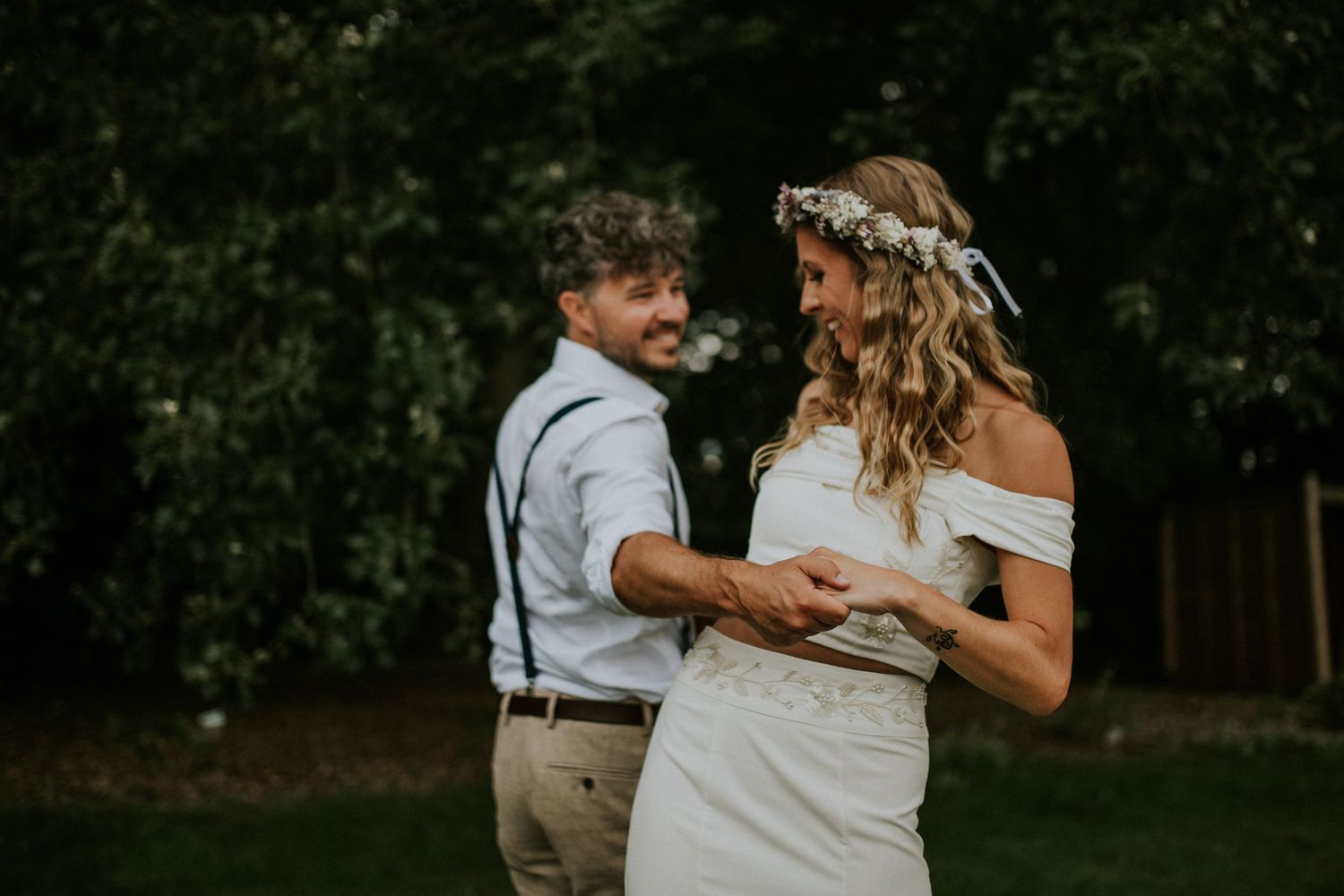 A romantic outdoor wedding moment captured against a dark natural backdrop with trees and greenery.