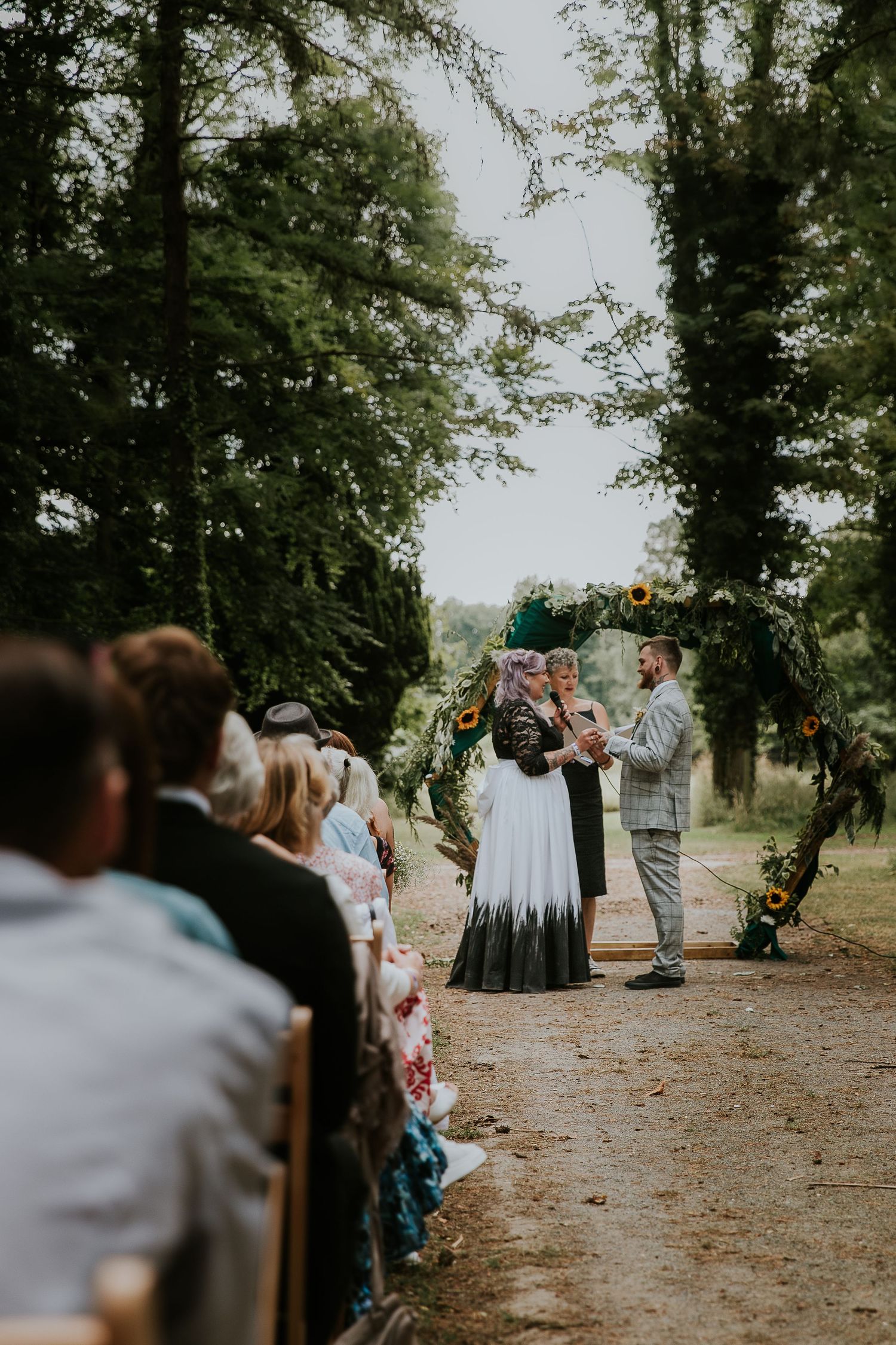 Wedding ceremony in wooded setting with guests seated along forest path.