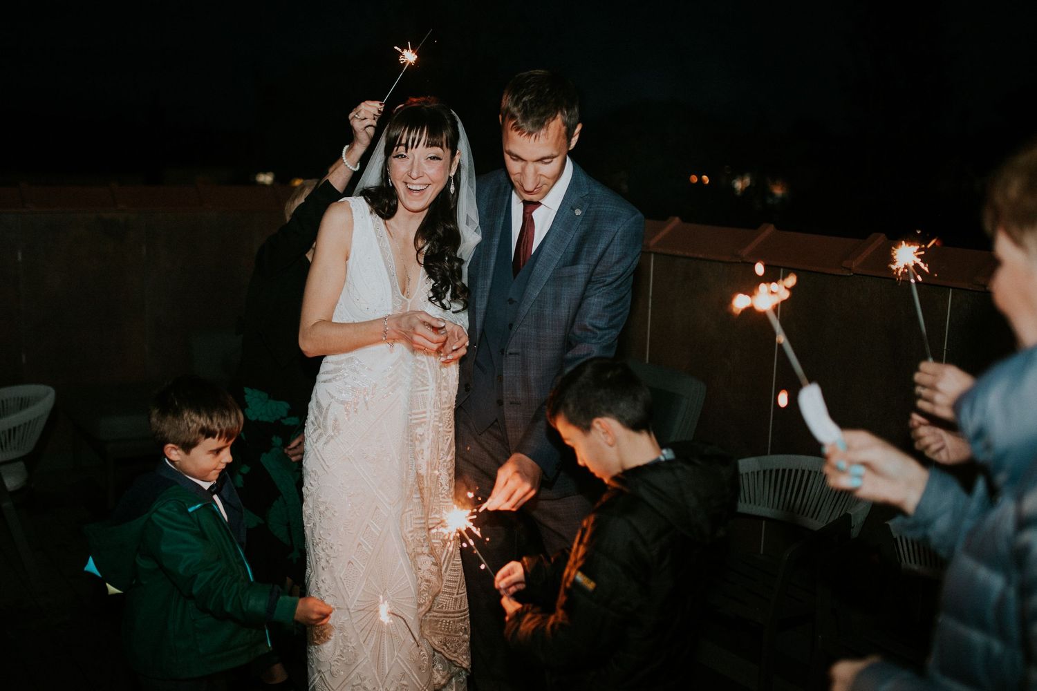 Couple and children celebrate with sparklers during evening wedding festivities.