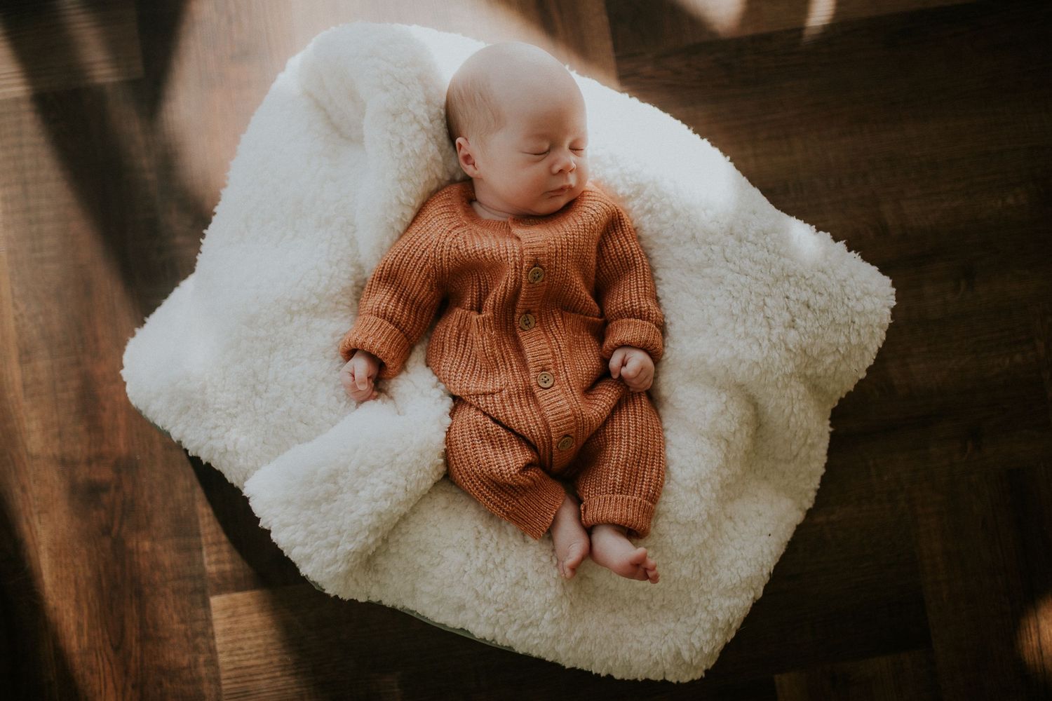 Newborn in brown clothing rests on soft white blanket in moody lighting.