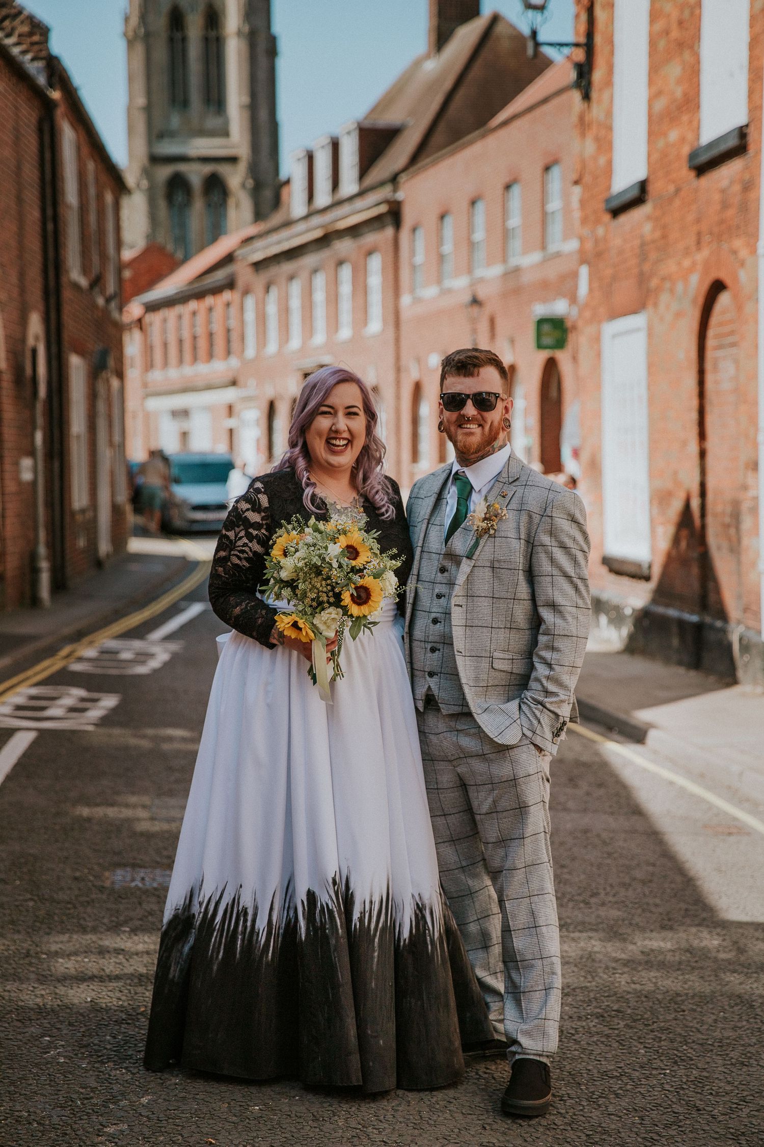Couple poses on cobblestone street with church spire and historic buildings.
