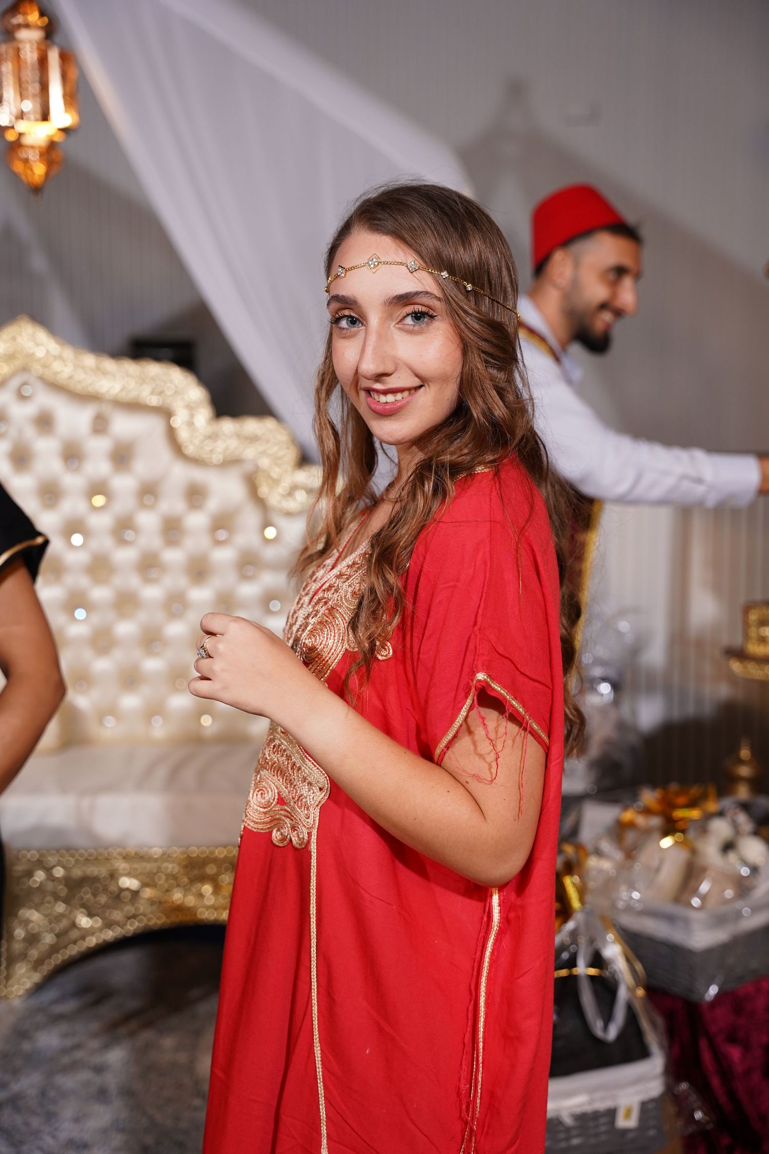 Woman in red outfit smiling against luxurious gold and white party decor.