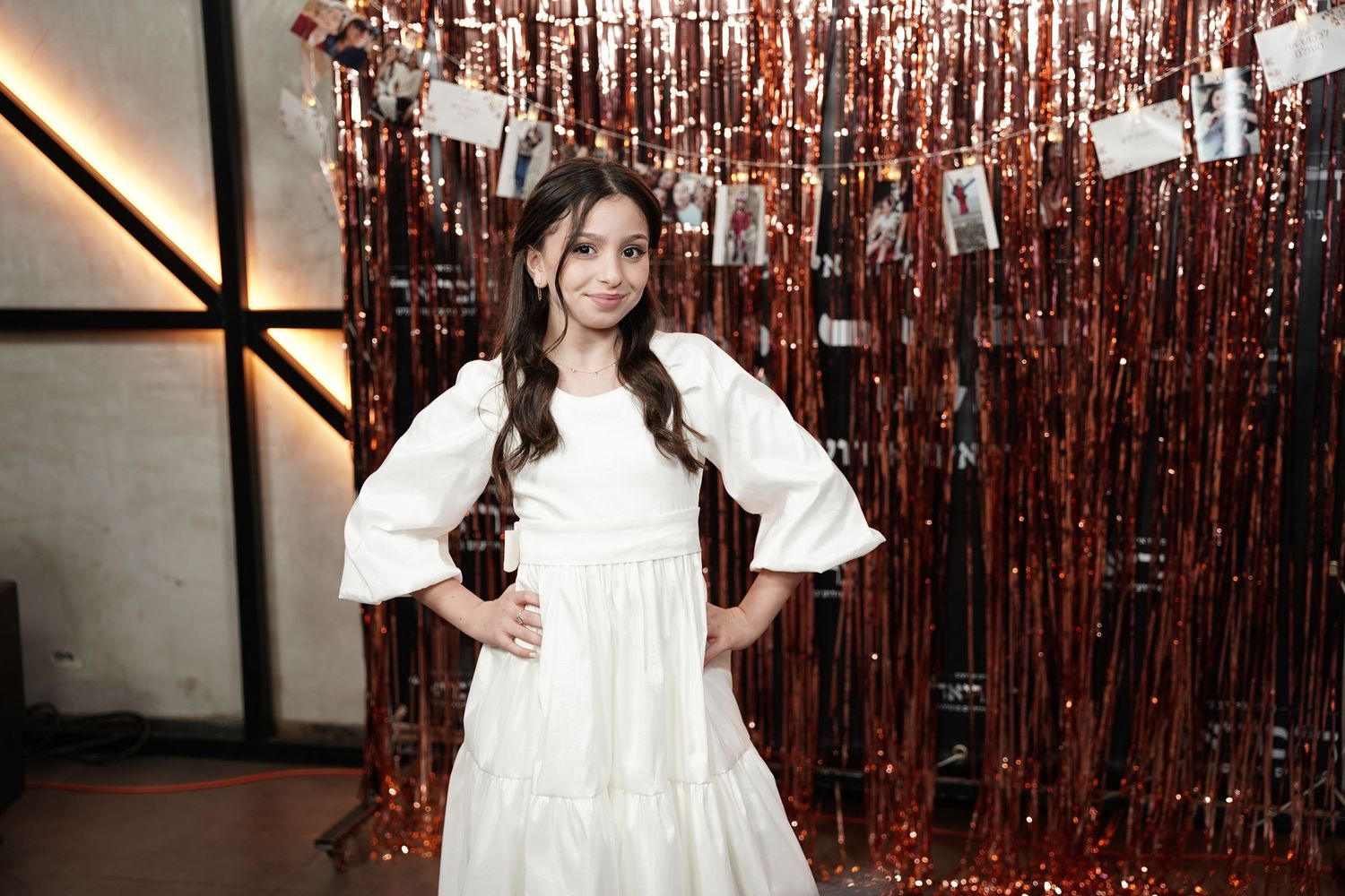 A person in a white ruffled dress poses in front of a rose gold metallic curtain backdrop.