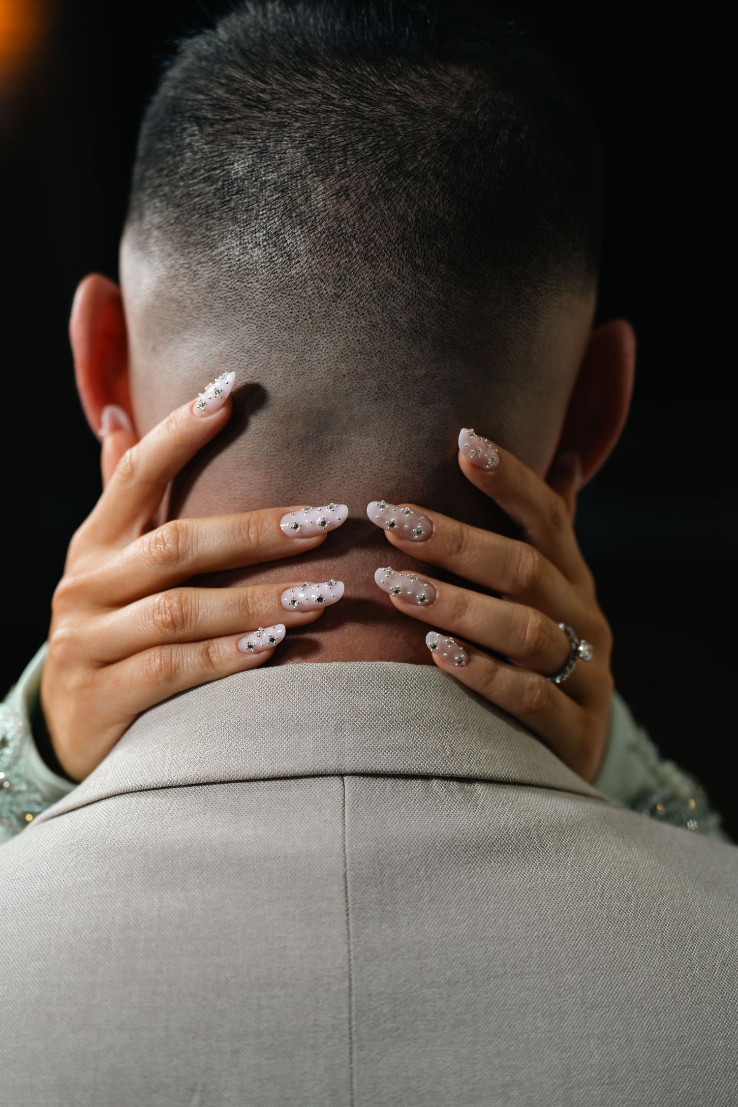 Close-up of manicured hands with floral nail art resting on the back of a man's neck in a beige suit.