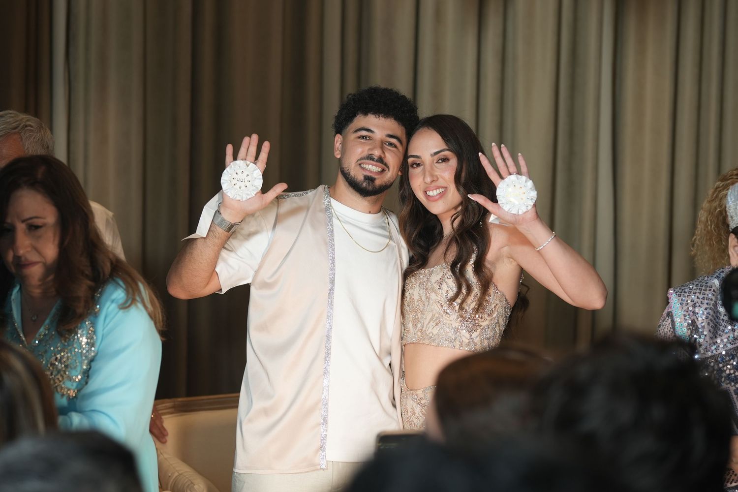 Couple in white outfits showing gloved hands at a festive celebration event.
