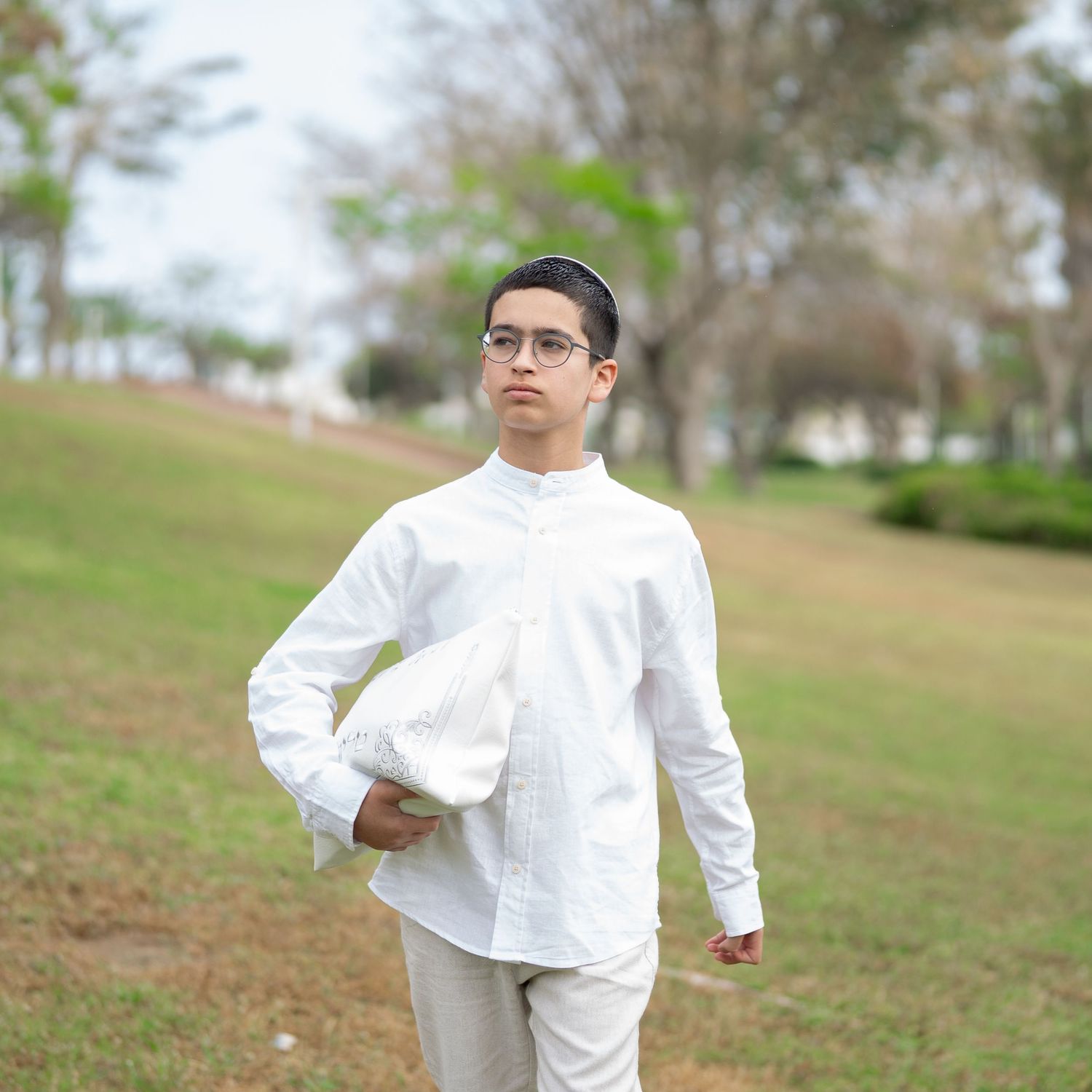 A figure in white clothing stands against a natural outdoor background.