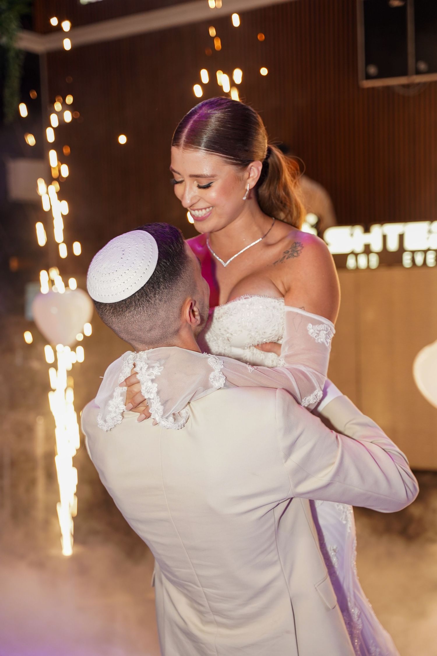 A couple shares their first dance surrounded by sparklers and fog effects on their wedding day.