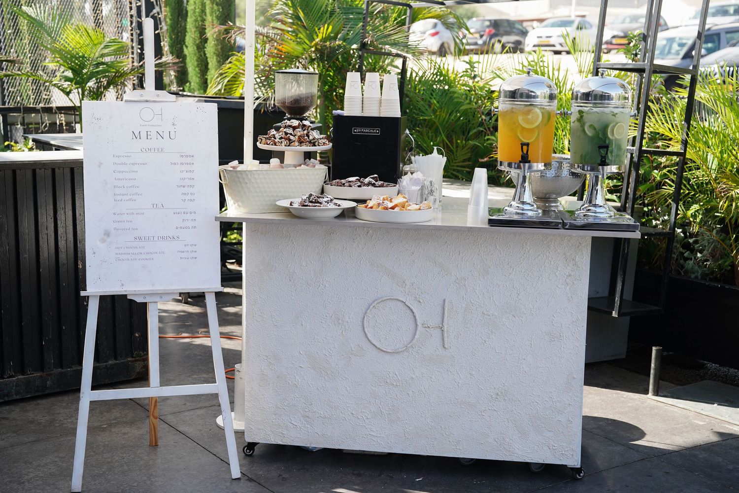 White event setup tables with decorations in an outdoor garden setting.
