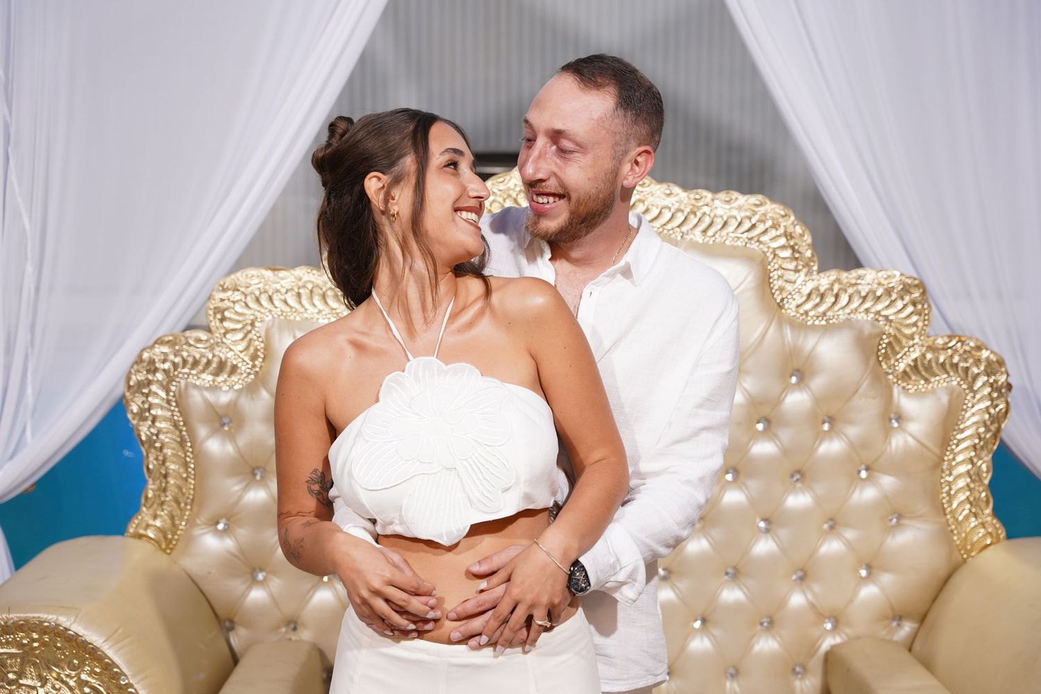 Couple embracing and laughing together in front of a luxurious tufted gold headboard.