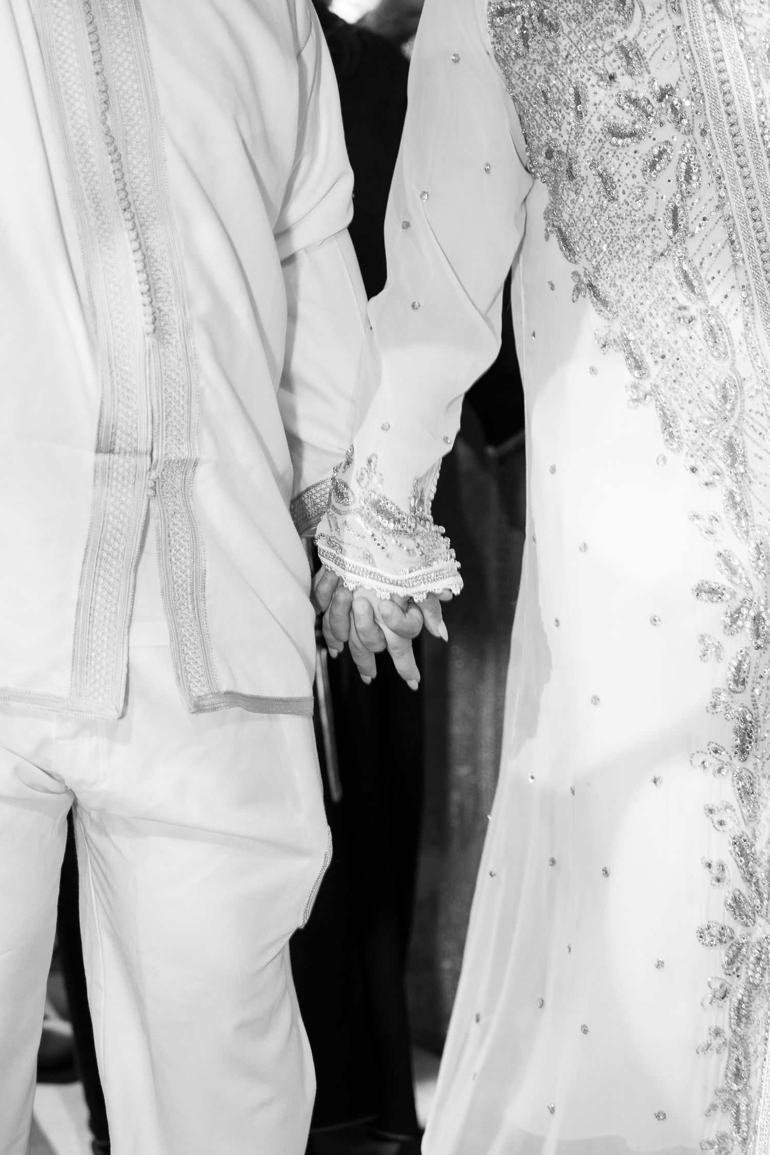 Black and white photo showing details of traditional white wedding attire with embroidery.