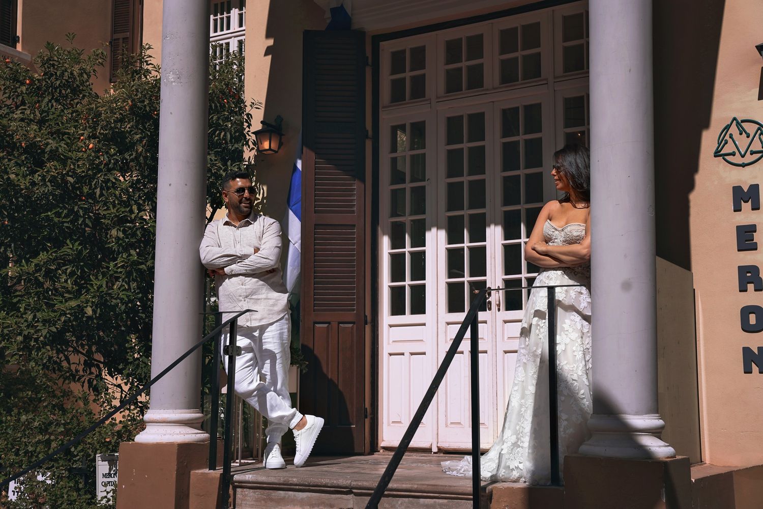 Two people in white outfits lean against columns on a building's front steps.