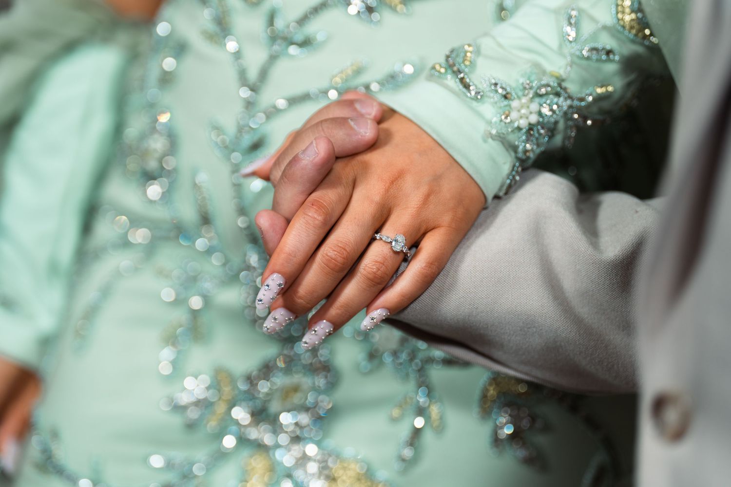Close-up of hands with glittery nails and a diamond ring, wearing a mint green beaded dress.