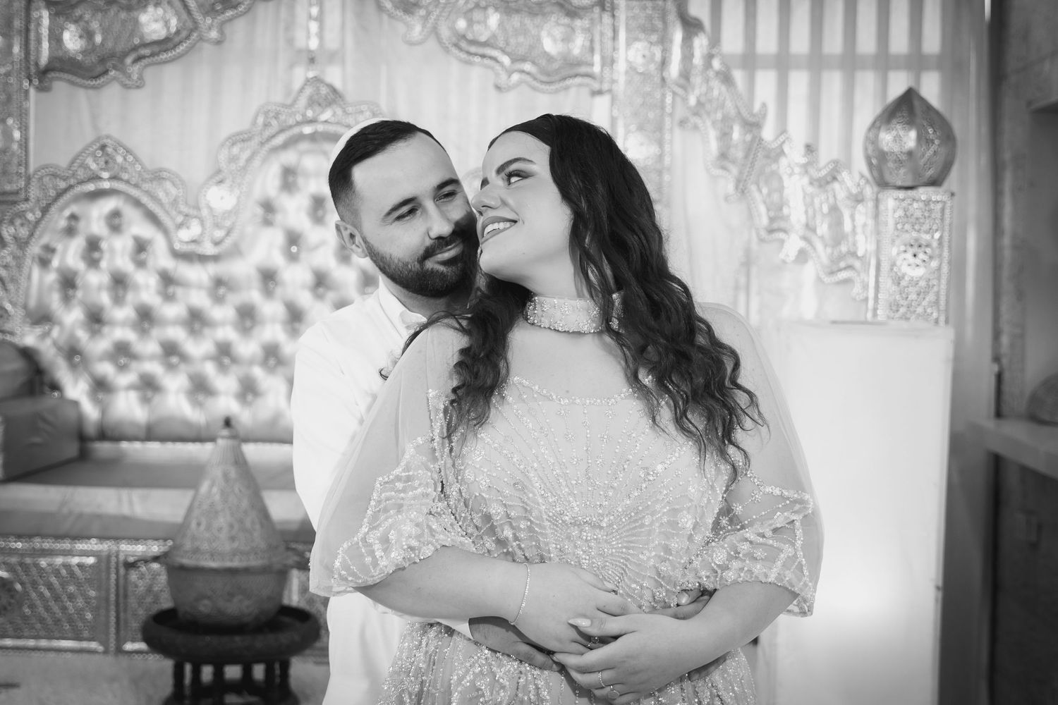 Black and white photo of couple embracing in front of decorative backdrop.