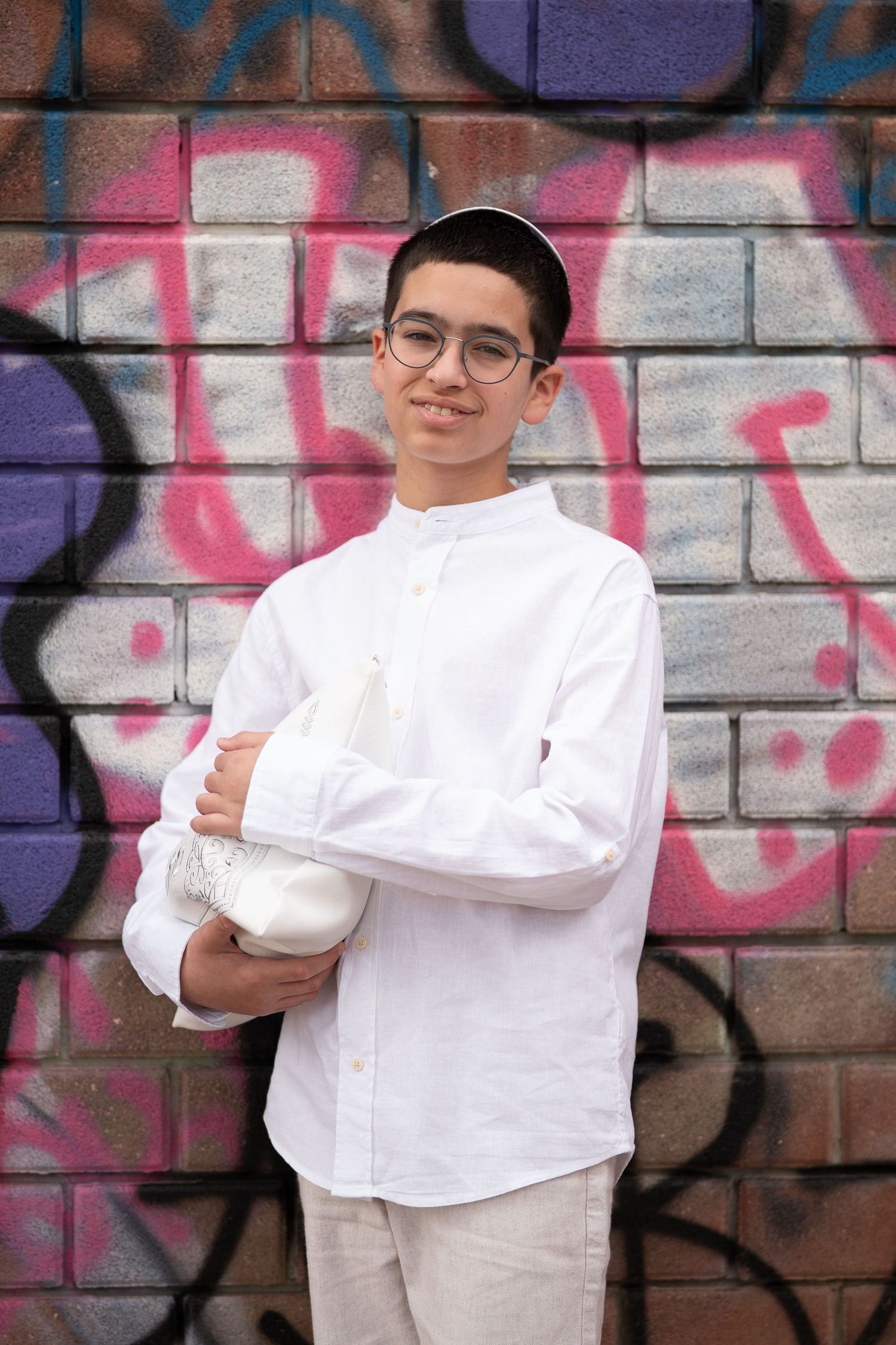 A person in white attire poses against a graffiti wall with colorful street art.