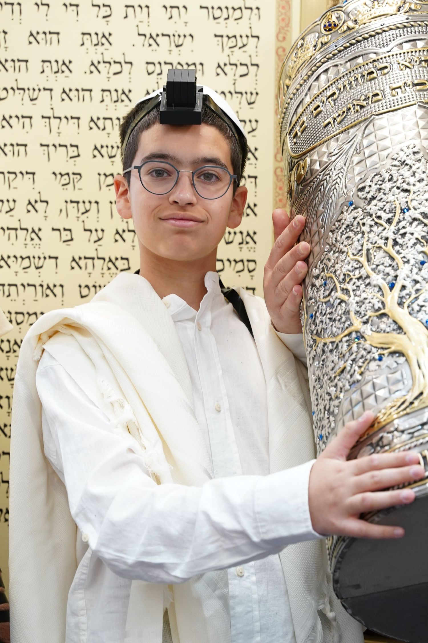 Person standing next to ornate Torah scrolls with Hebrew text visible.