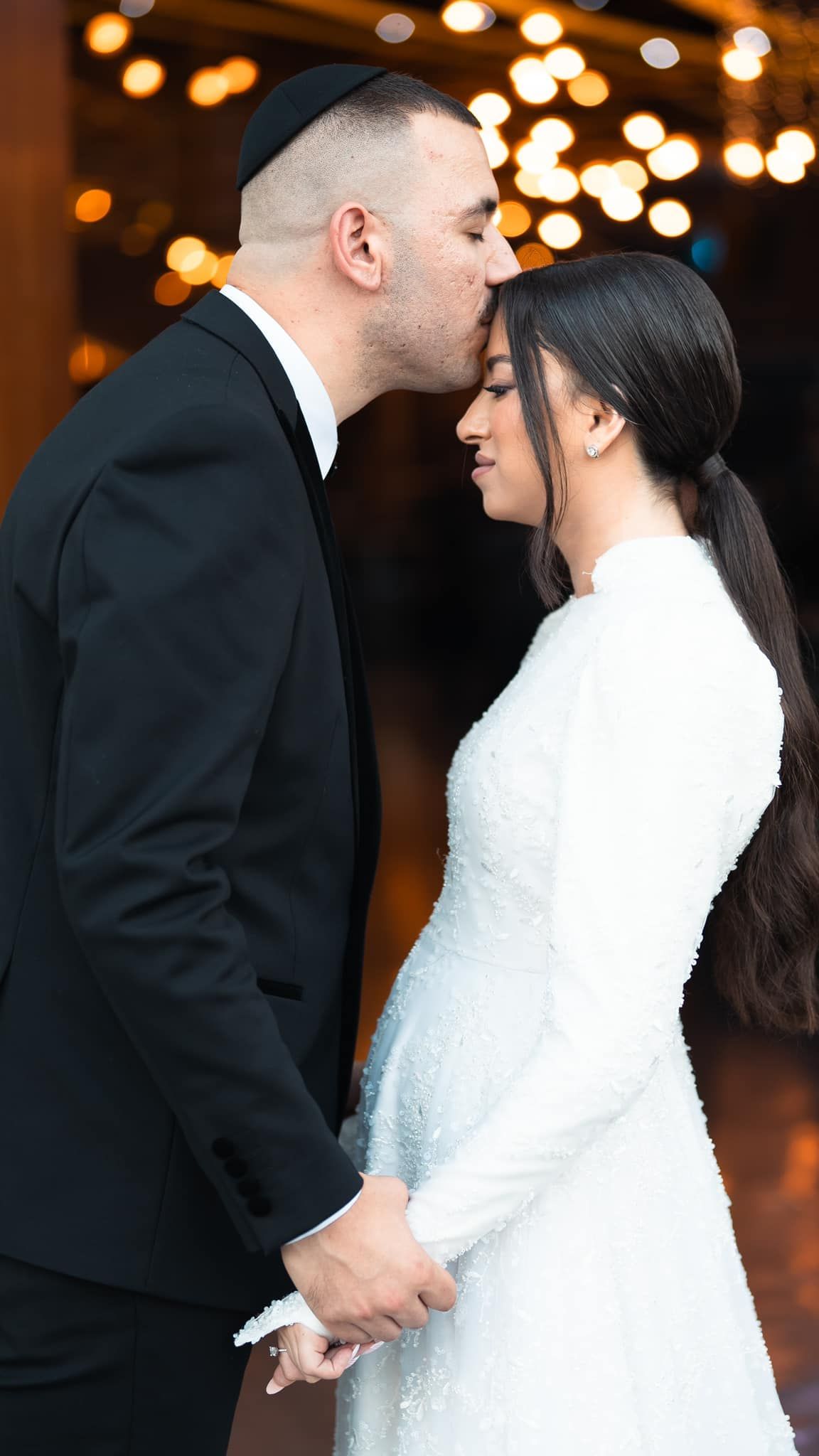 Intimate moment captured between newlyweds with warm bokeh lighting in background.