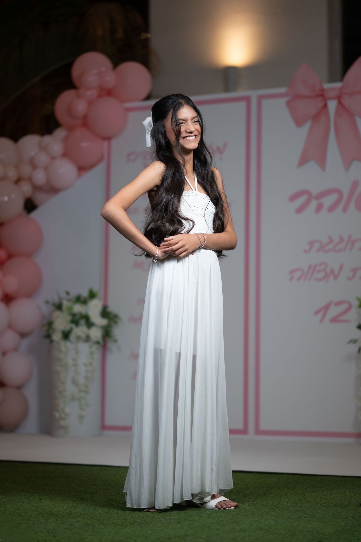 A flowing white dress photographed against a pink and white decorated backdrop with balloons.