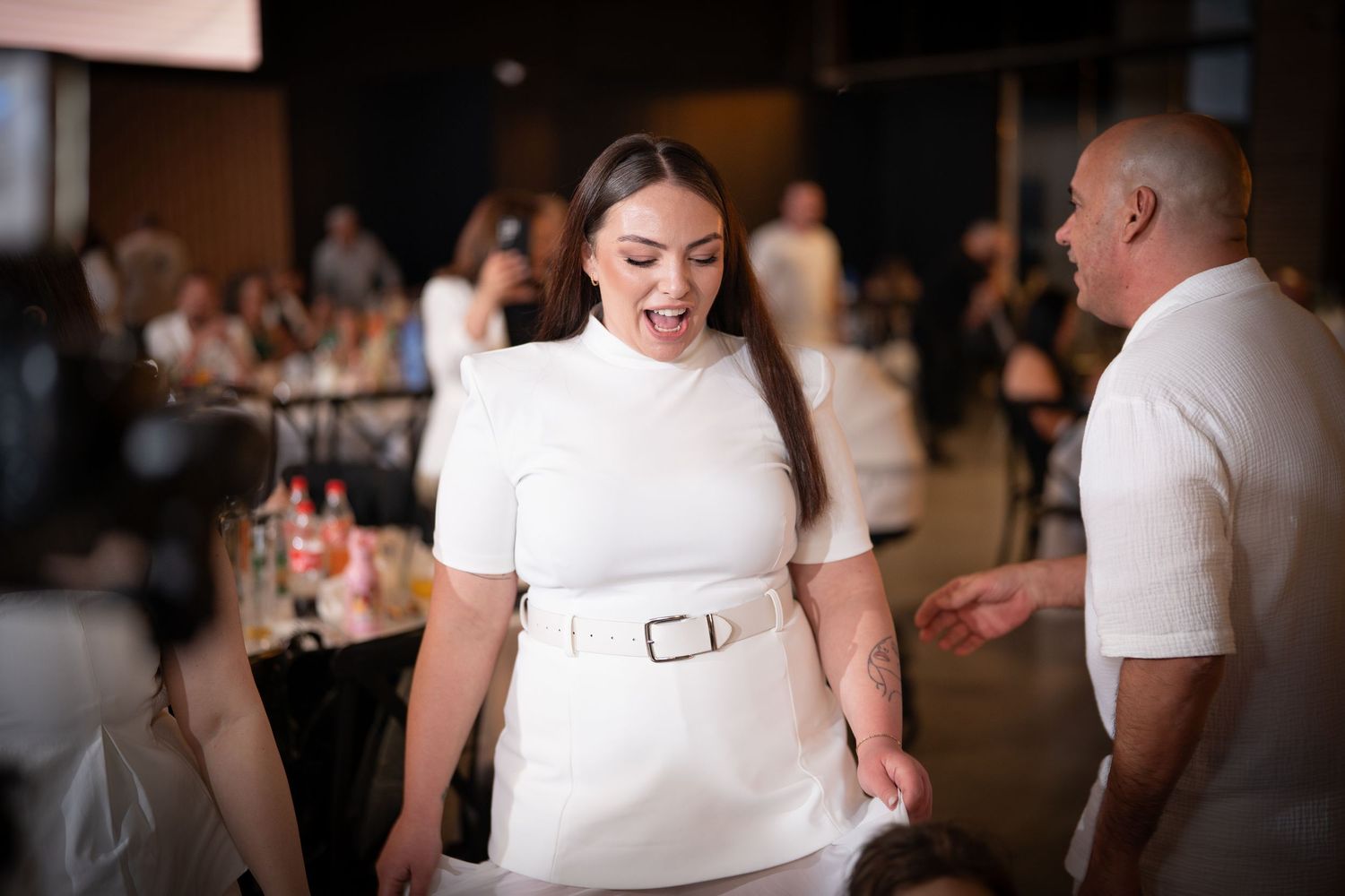 Indoor celebration with white-clad attendees enjoying festivities under ambient lighting.