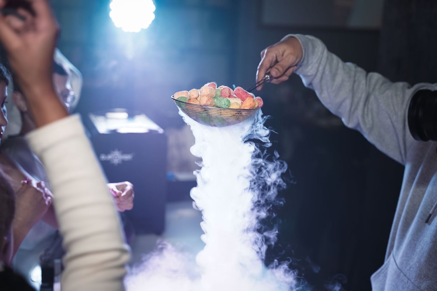A person exhales vapor clouds while holding an electronic cigarette in a dimly lit environment.