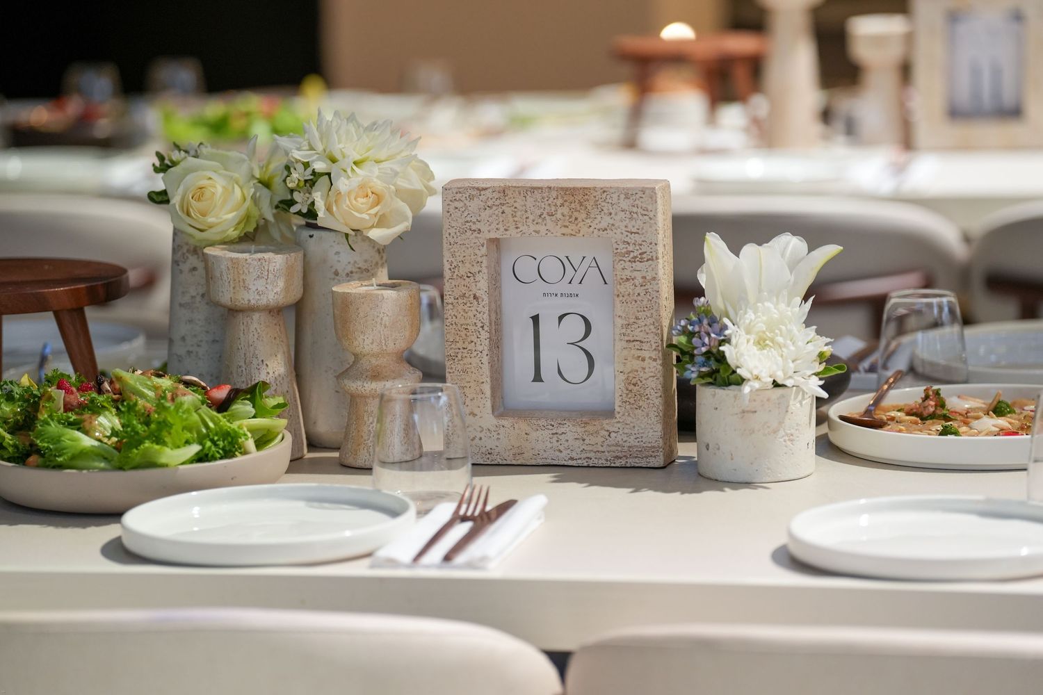 A rustic wedding reception table setting with white plates, wine glasses, and elegant table numbers.