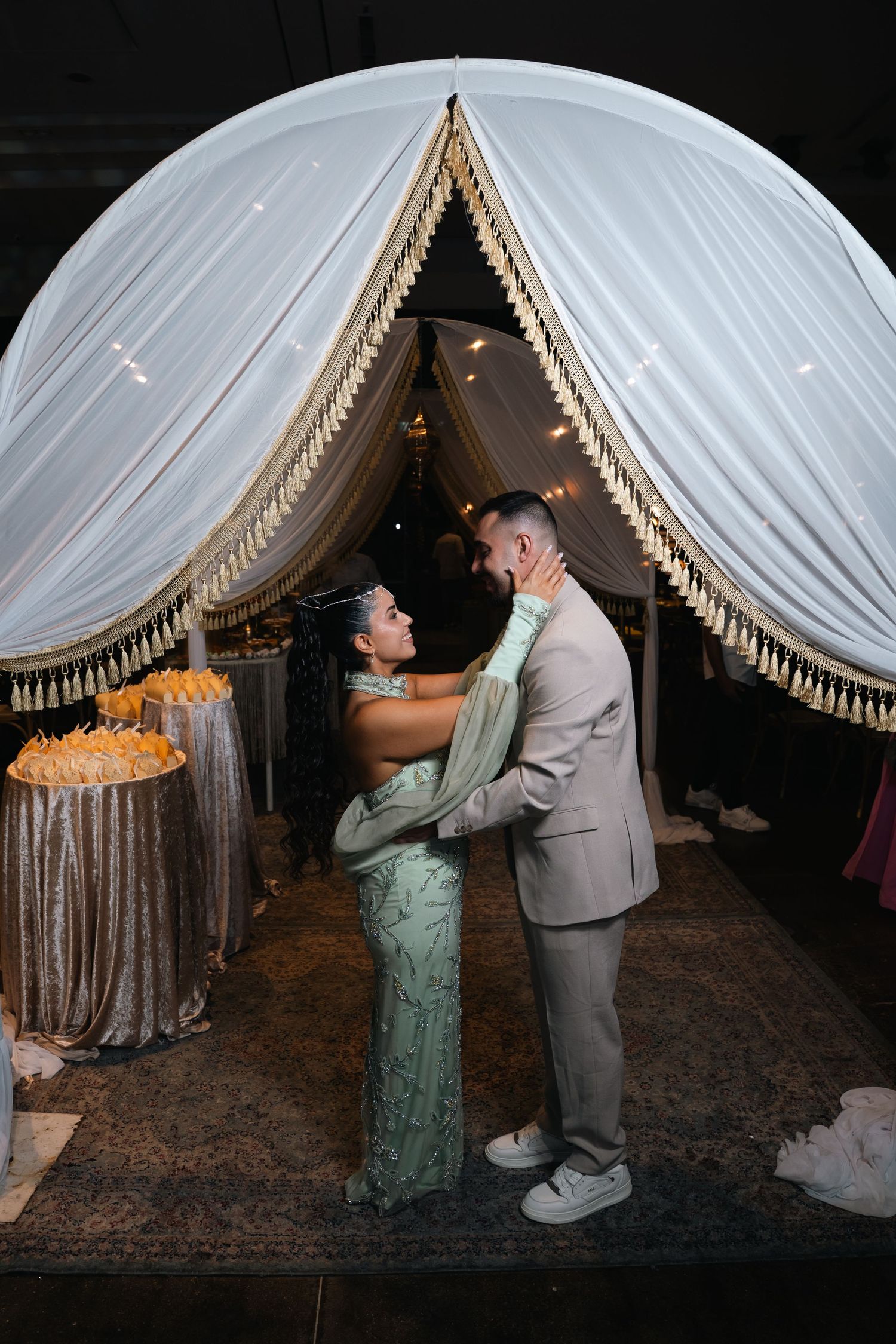 Couple sharing a romantic first dance under an elegant white draped arch with gold fringe at a formal wedding reception.