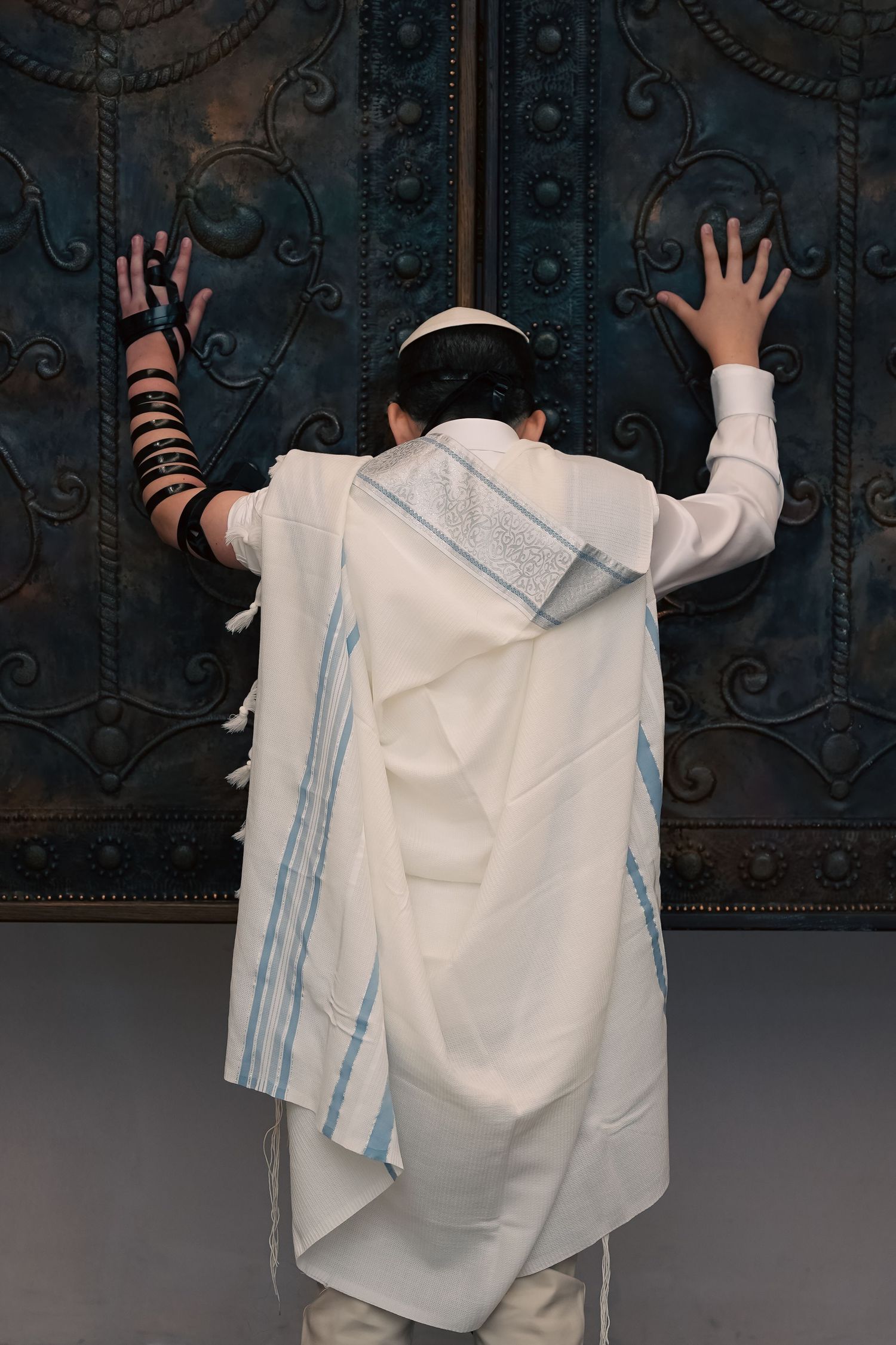 Person wearing flowing white ceremonial garment with blue details against dark background.