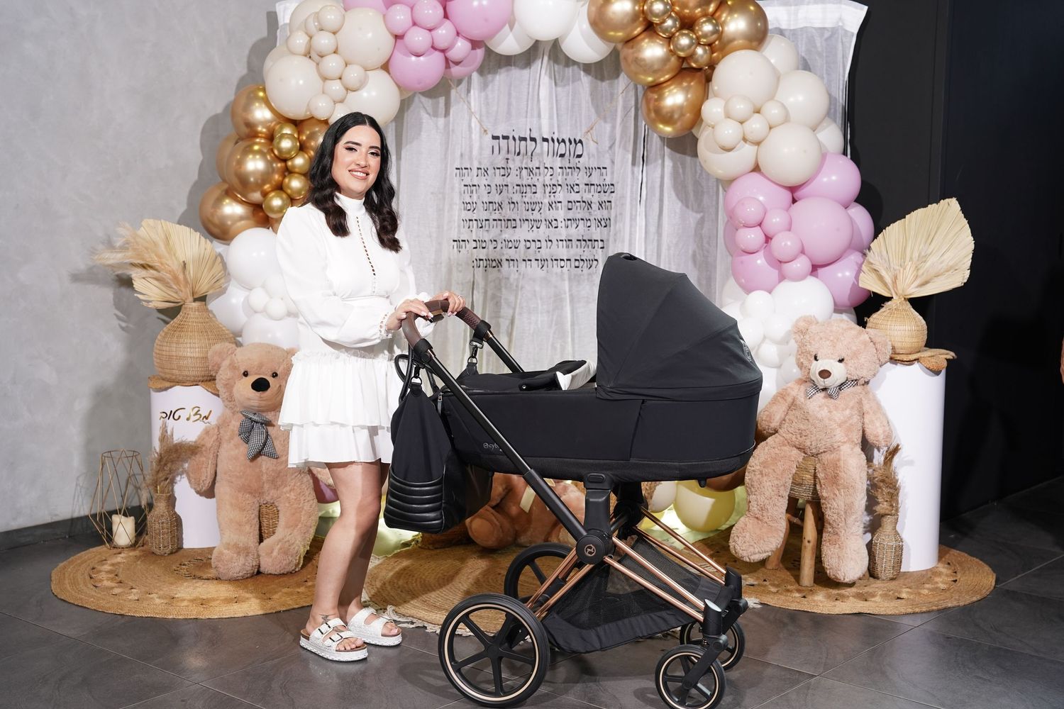 Baby shower decoration featuring pink and gold balloons with plush teddy bears and a stroller.