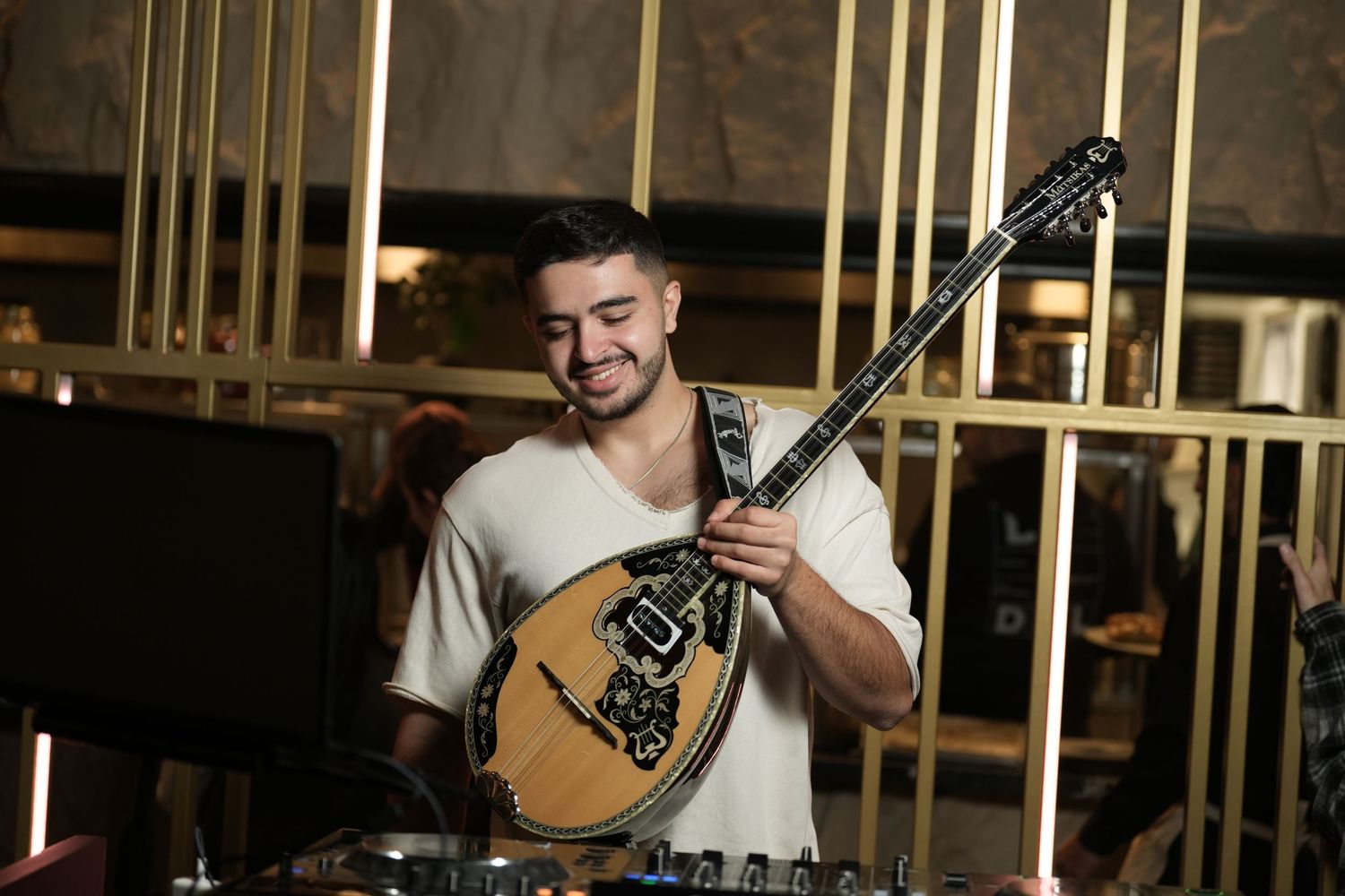 Musician performs on stage with a traditional mandolin instrument against a dark background with vertical lighting elements.