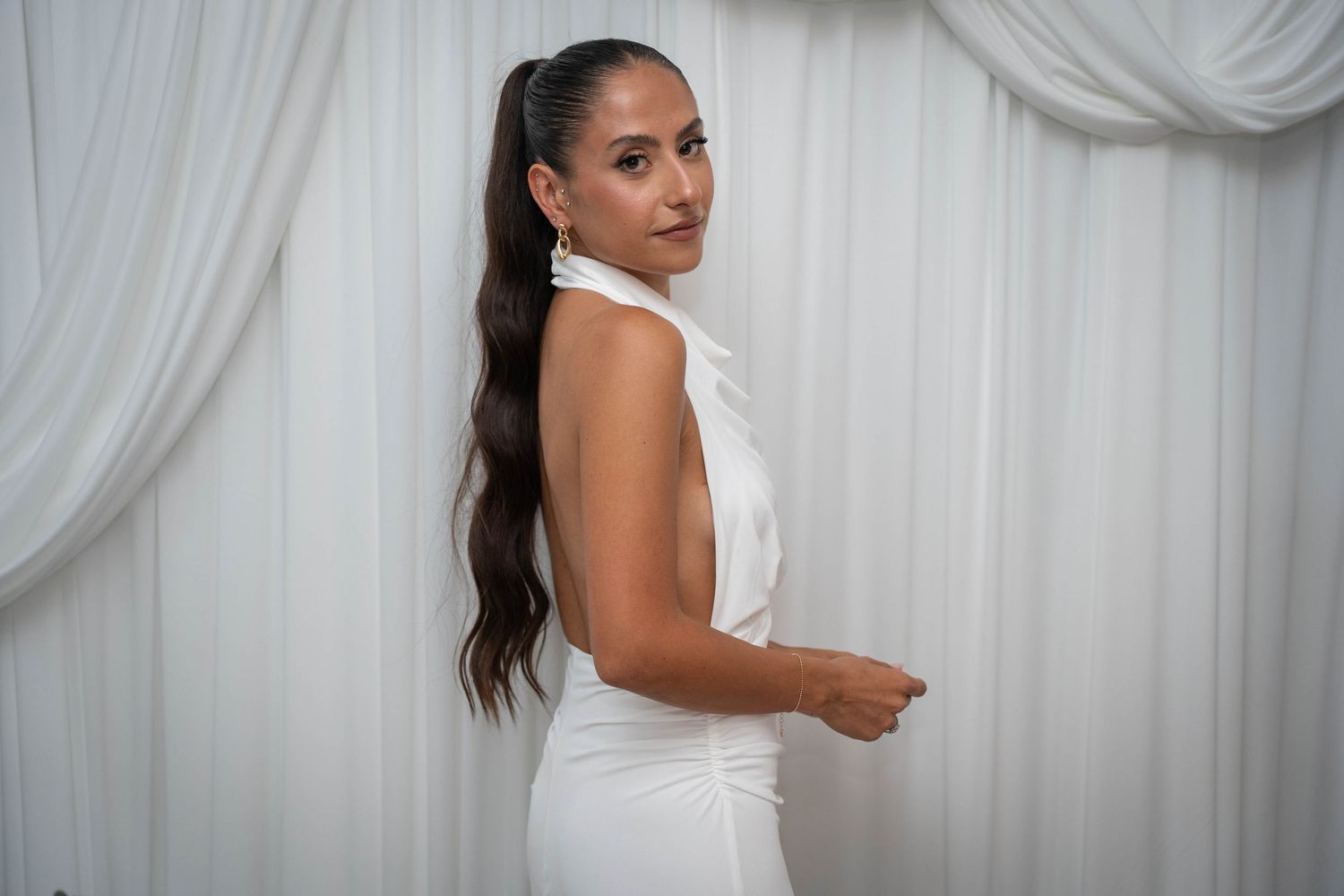 Woman in white dress posing against draped fabric backdrop at formal event.
