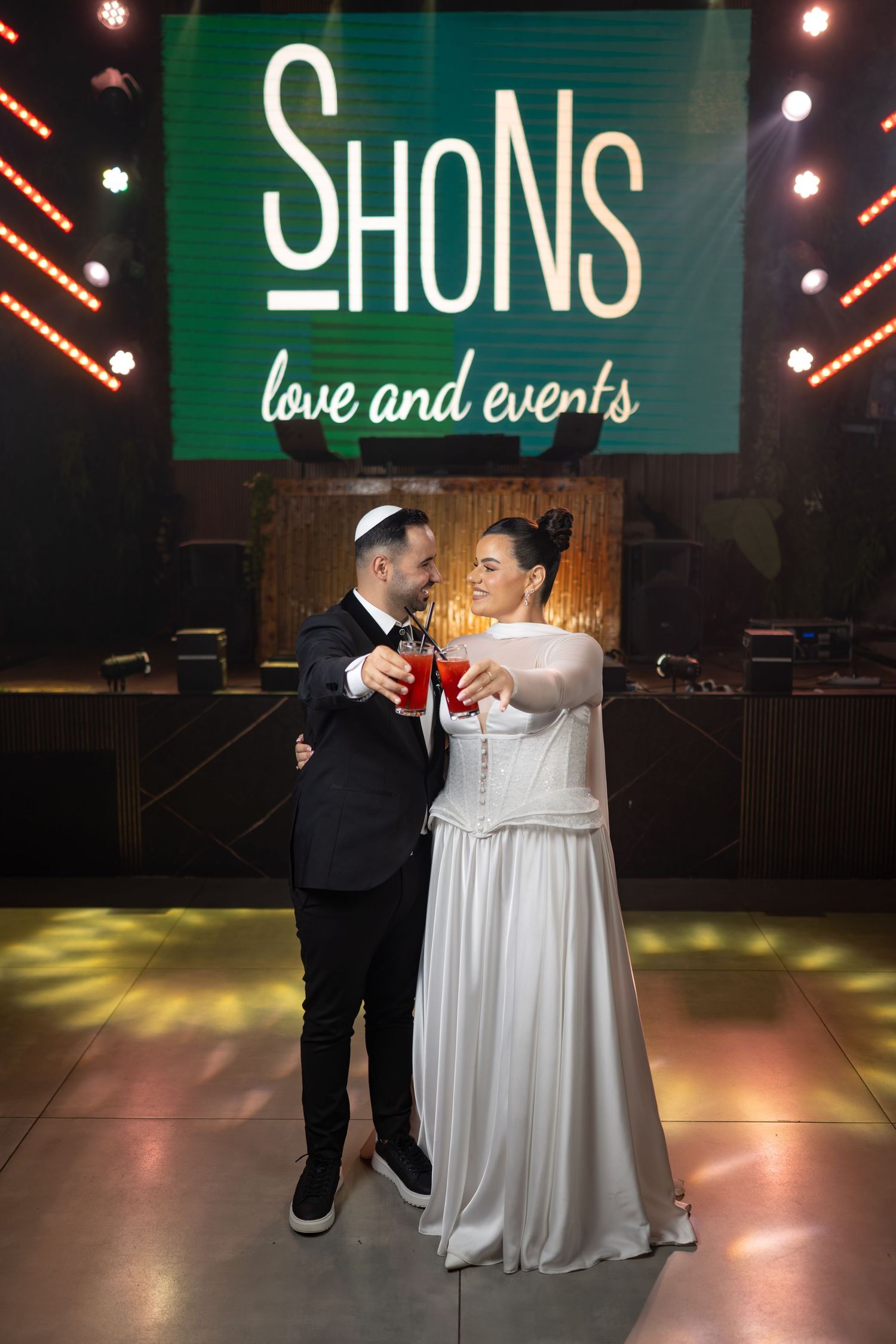 Wedding couple dancing under green neon signage in a modern venue setting.