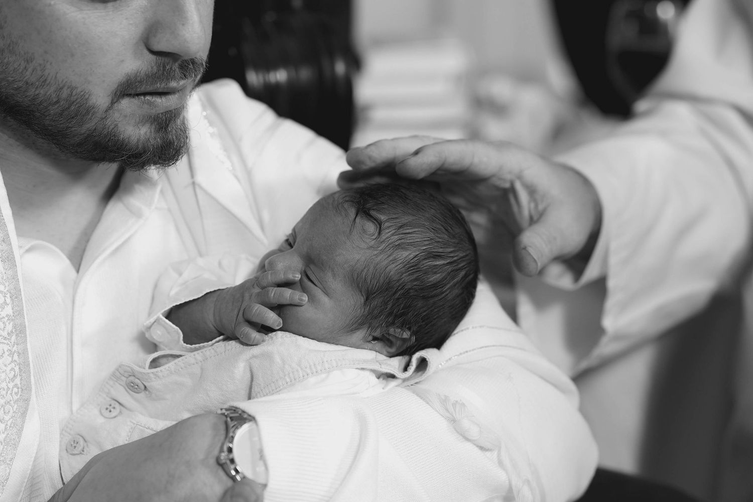 Black and white intimate portrait of a newborn being cradled in white clothing.