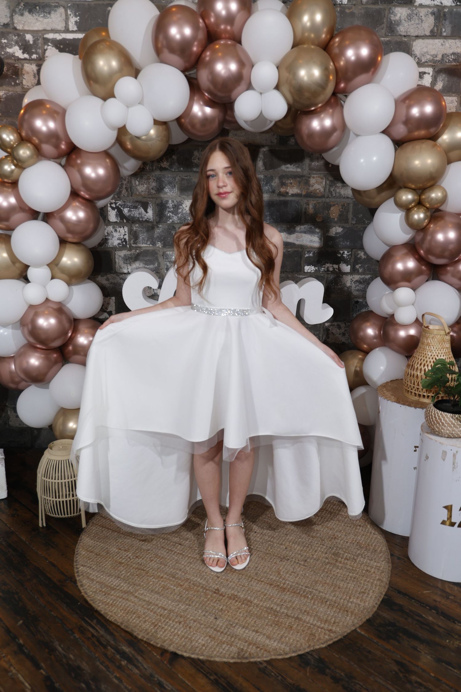 White dress photoshoot with balloon decorations and rustic brick wall backdrop.