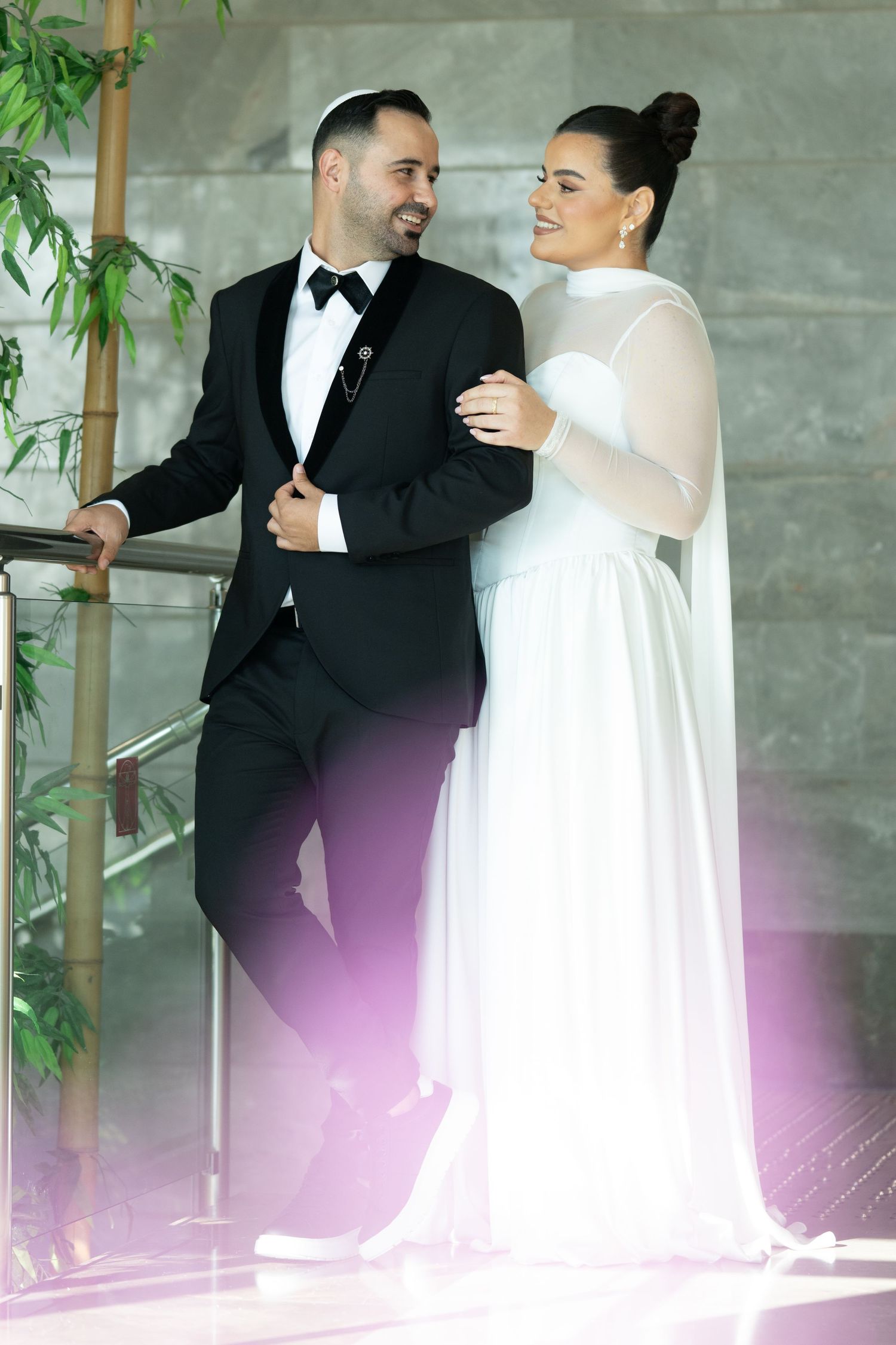A couple poses together on stairs, wearing formal wedding attire in a modern indoor setting.