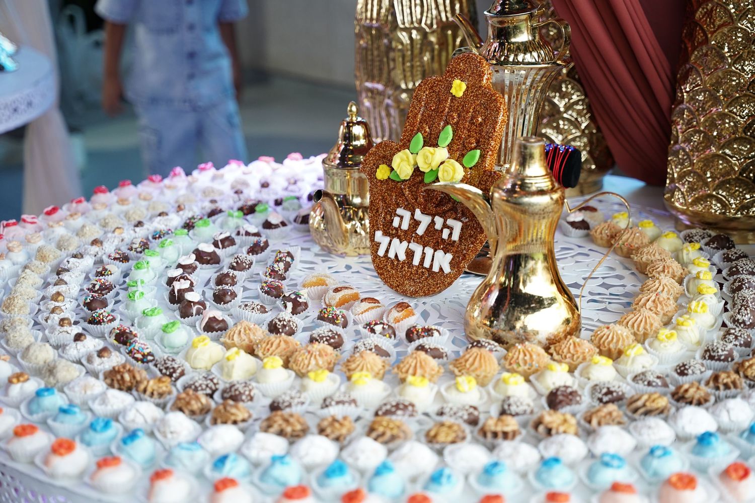 Elaborate Jewish celebration table with colorful candies, gold decorations, and Hebrew text centerpiece.