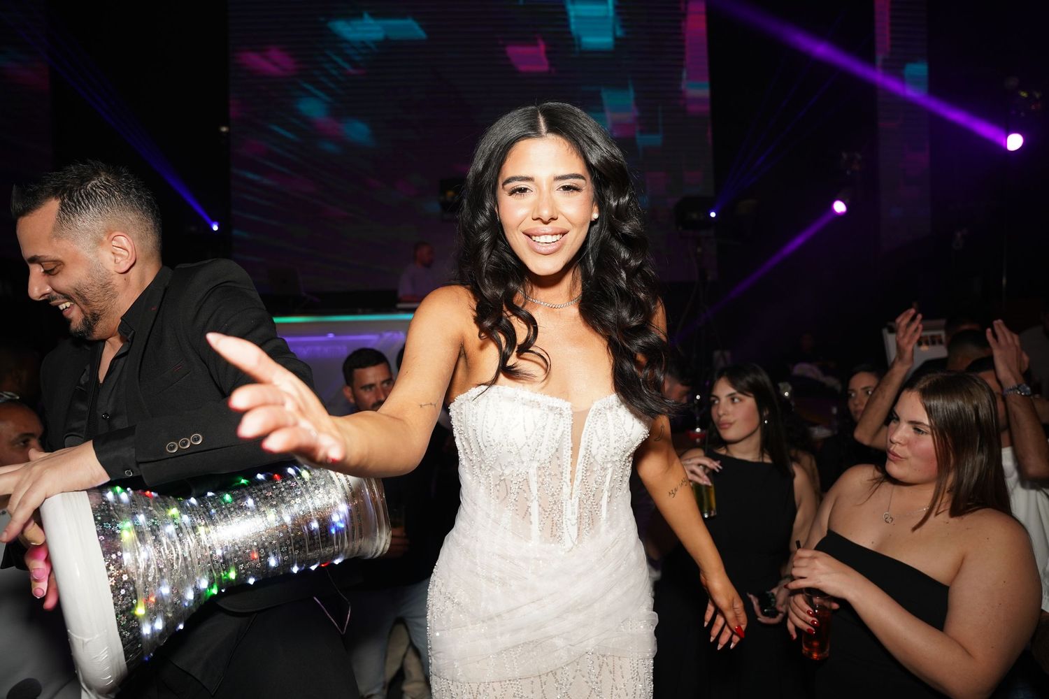 Lively wedding reception scene with guests dancing under purple and blue lighting.