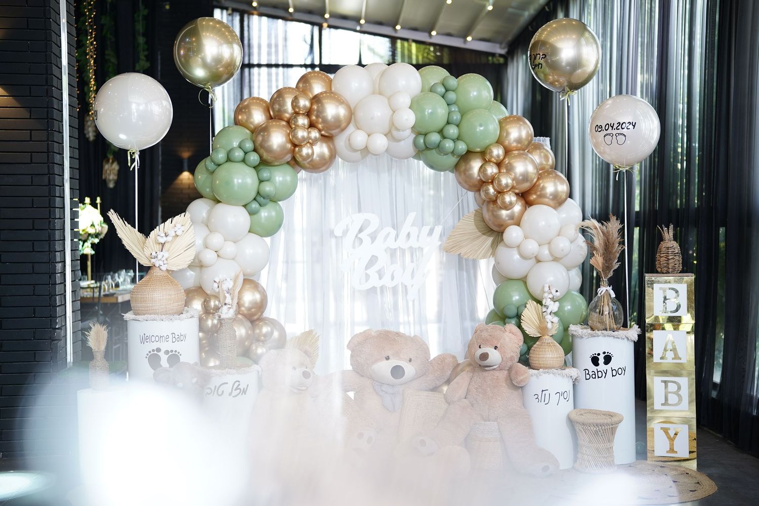 Elegant balloon arch with gold, white and sage green balloons decorating an indoor space.