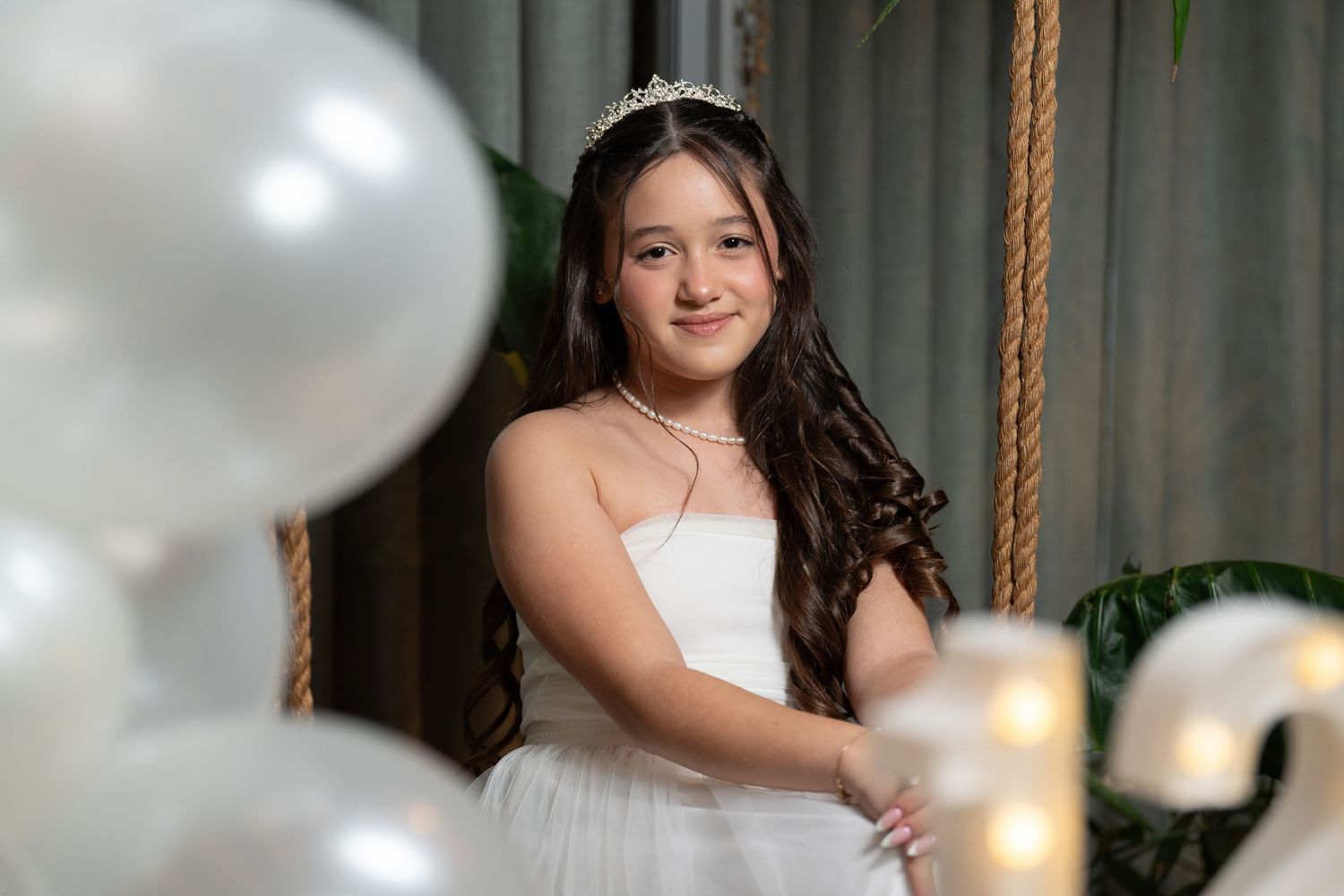 A bride in a white wedding dress poses with hanging decorative lights and ropes in a rustic indoor setting.