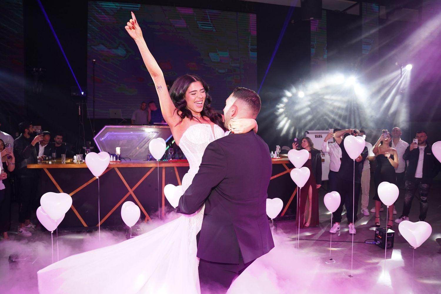 Wedding reception dance floor illuminated with purple lighting and heart-shaped decorations overhead.