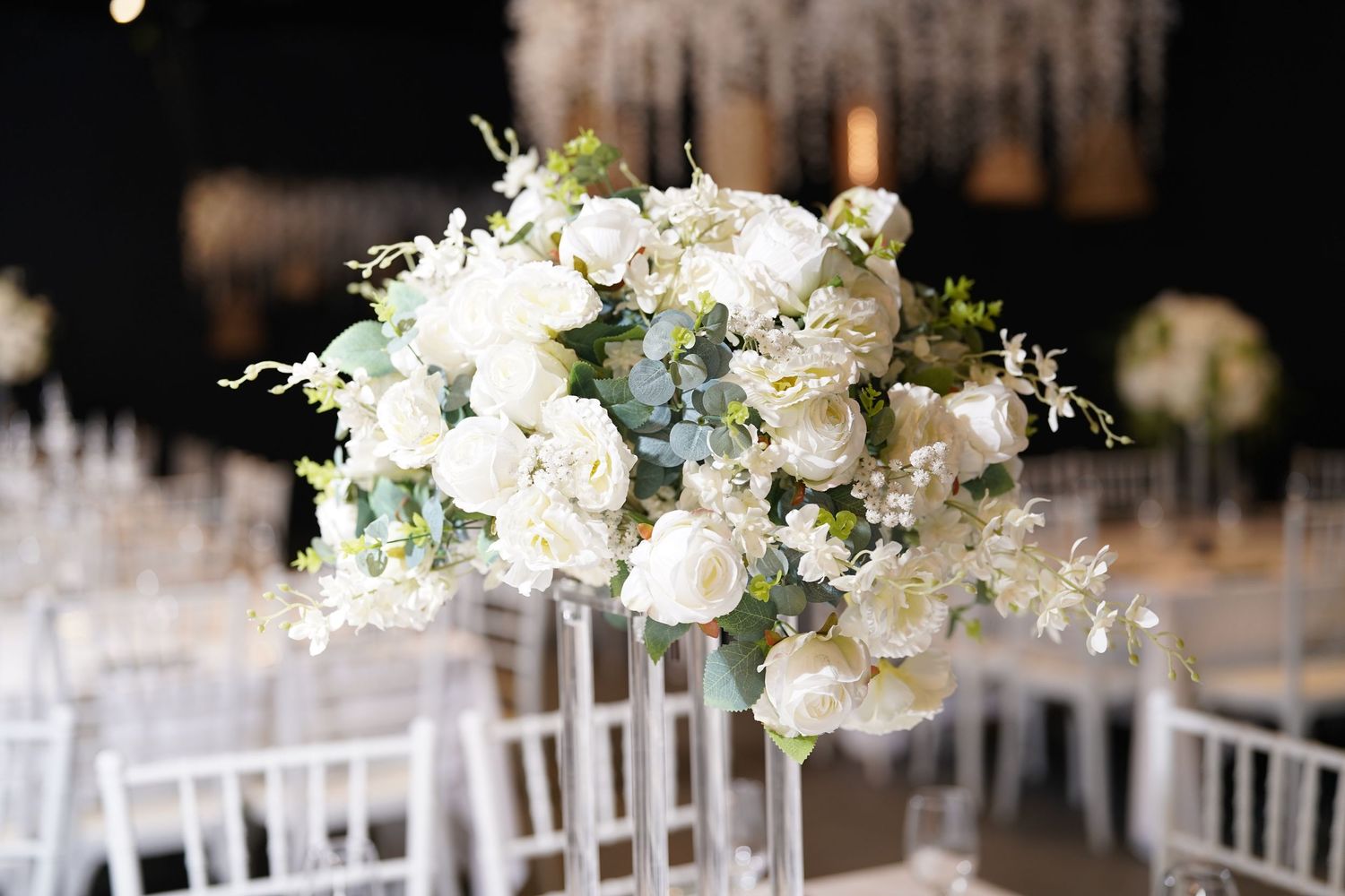 Elegant white floral centerpieces with crystal glassware on wedding reception tables.