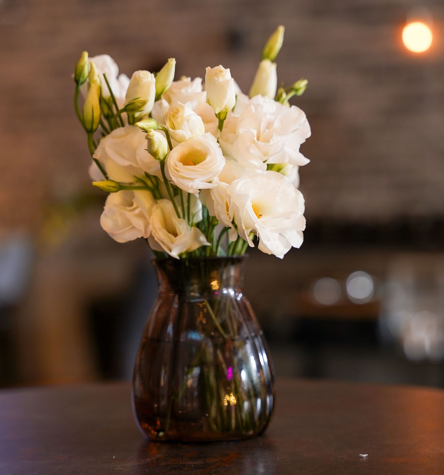 Delicate peach and cream flowers arranged in dark glass vases on wooden tables.